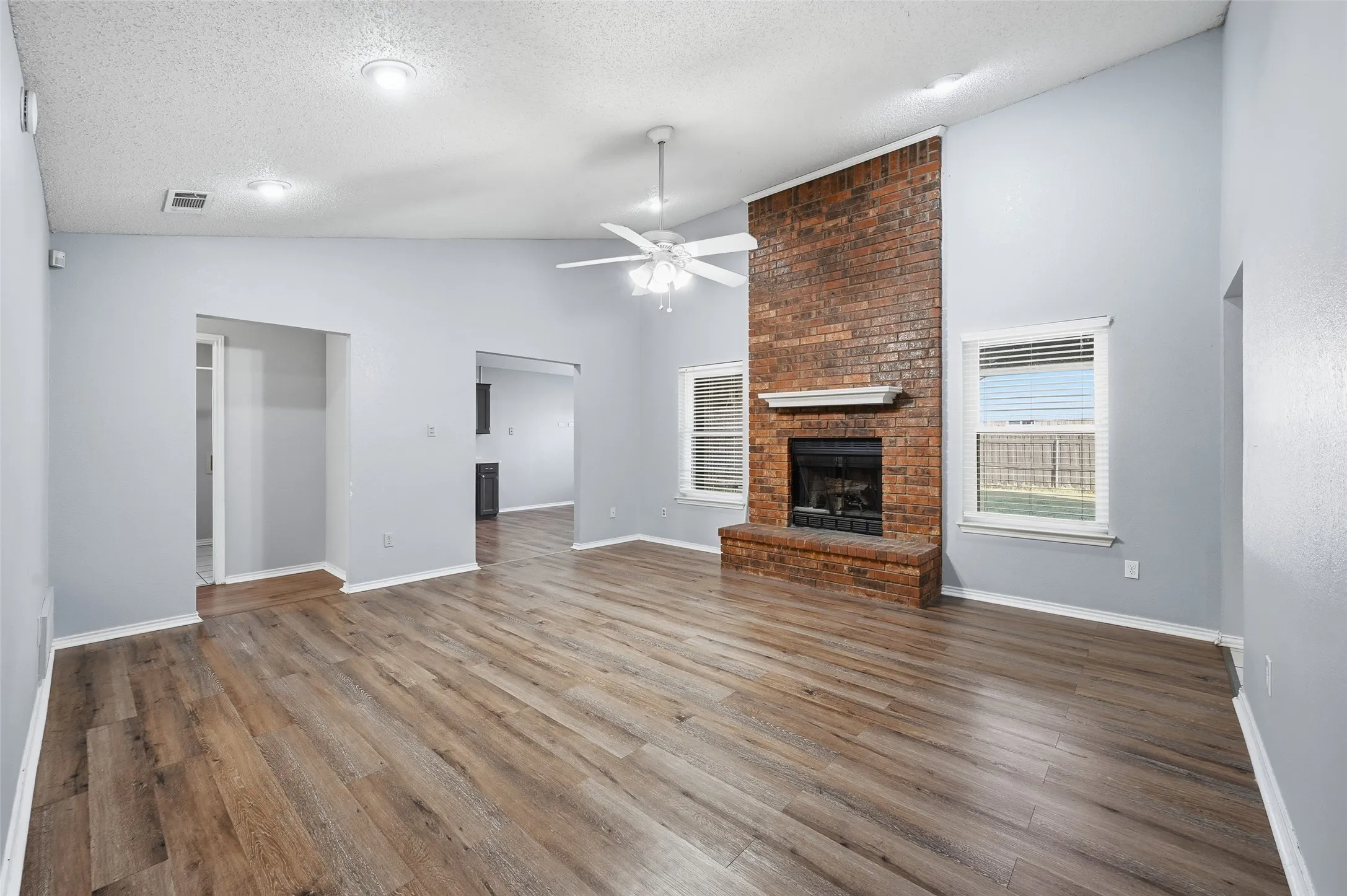 Vaulted ceiling, wood-finish flooring, brick fireplace with a white mantel, ceiling fan, and recessed lighting