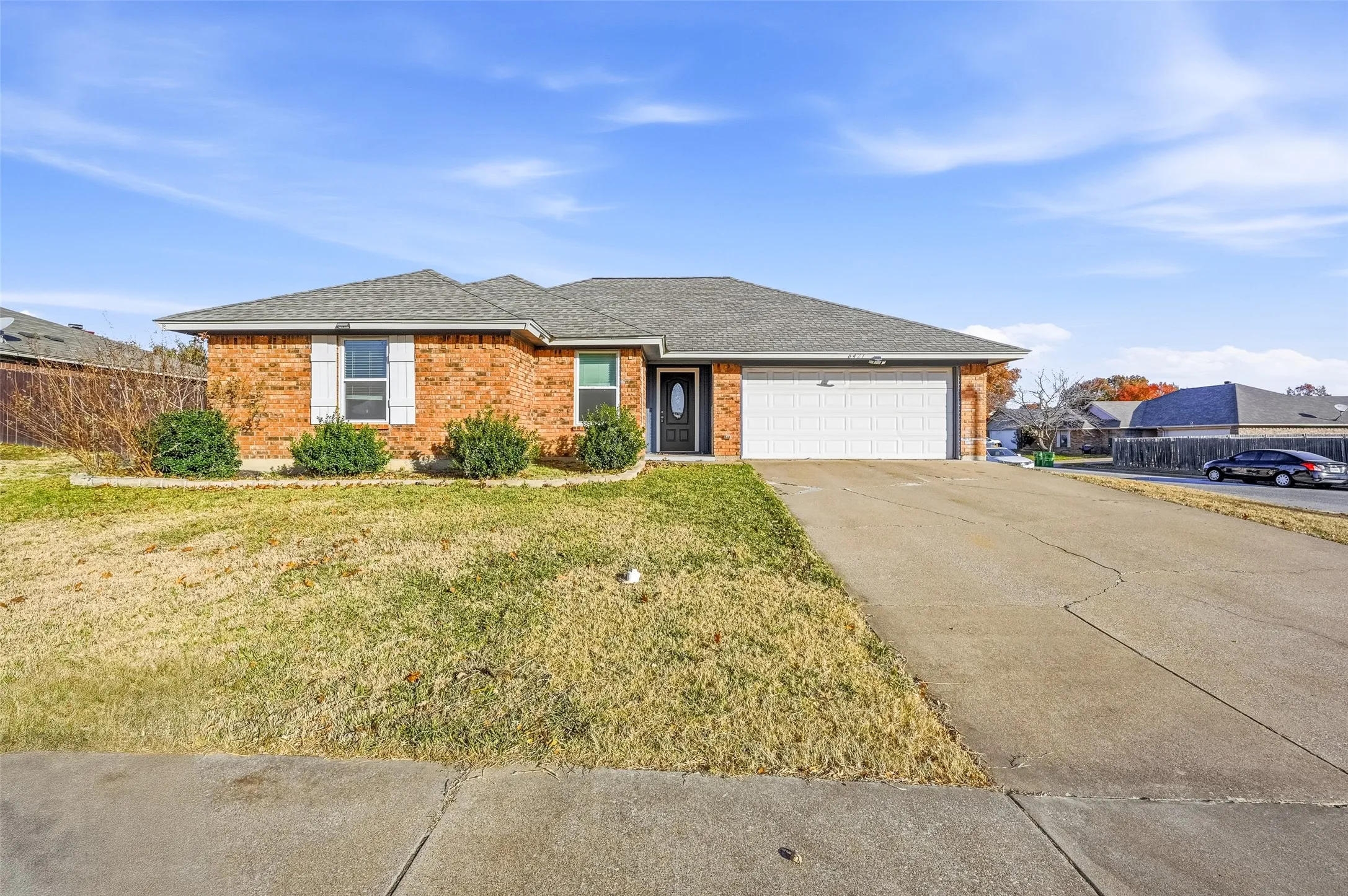 Brick exterior with a gray shingle roof, attached two-car garage, concrete driveway, and front landscaping