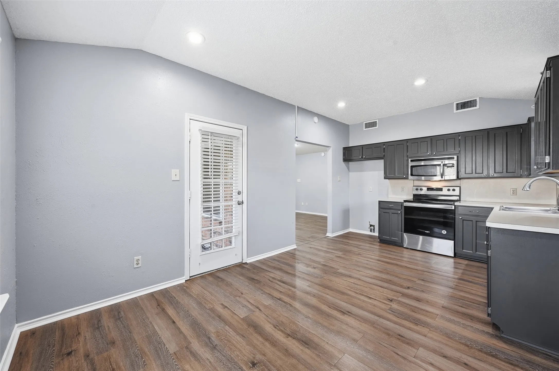 Wood-finish flooring, recessed lighting, and a kitchen featuring dark cabinetry with stainless steel appliances and light countertops