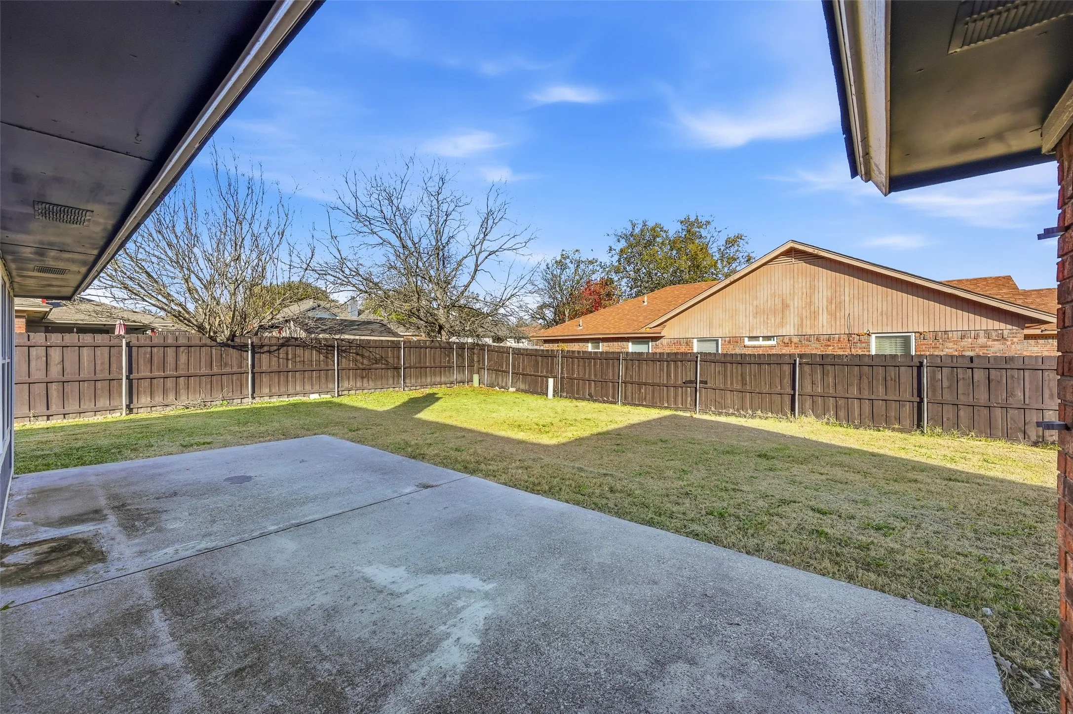 Expansive backyard featuring a concrete patio, a manicured lawn, and a wood privacy fence
