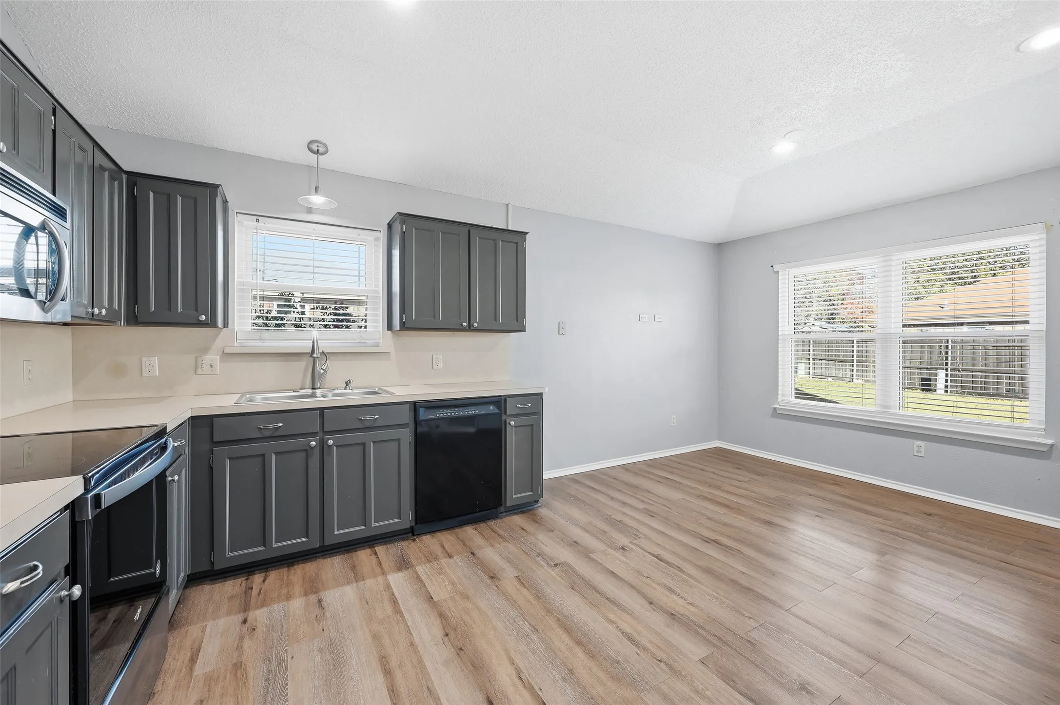Kitchen featuring grey cabinetry, stainless steel appliances, light countertops, and wood-finish flooring
