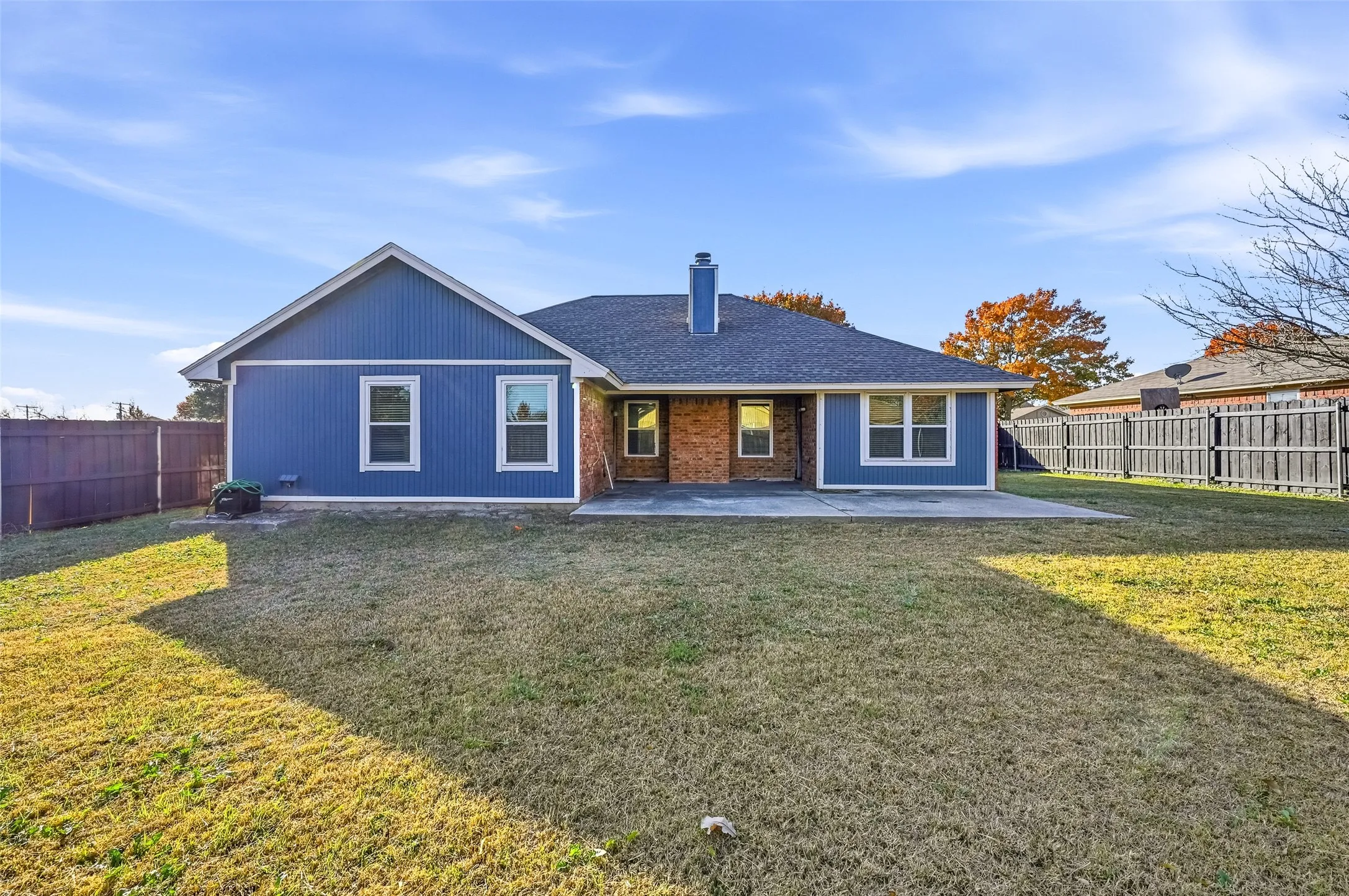 Expansive backyard featuring a concrete patio, wood privacy fencing, and a brick and siding exterior