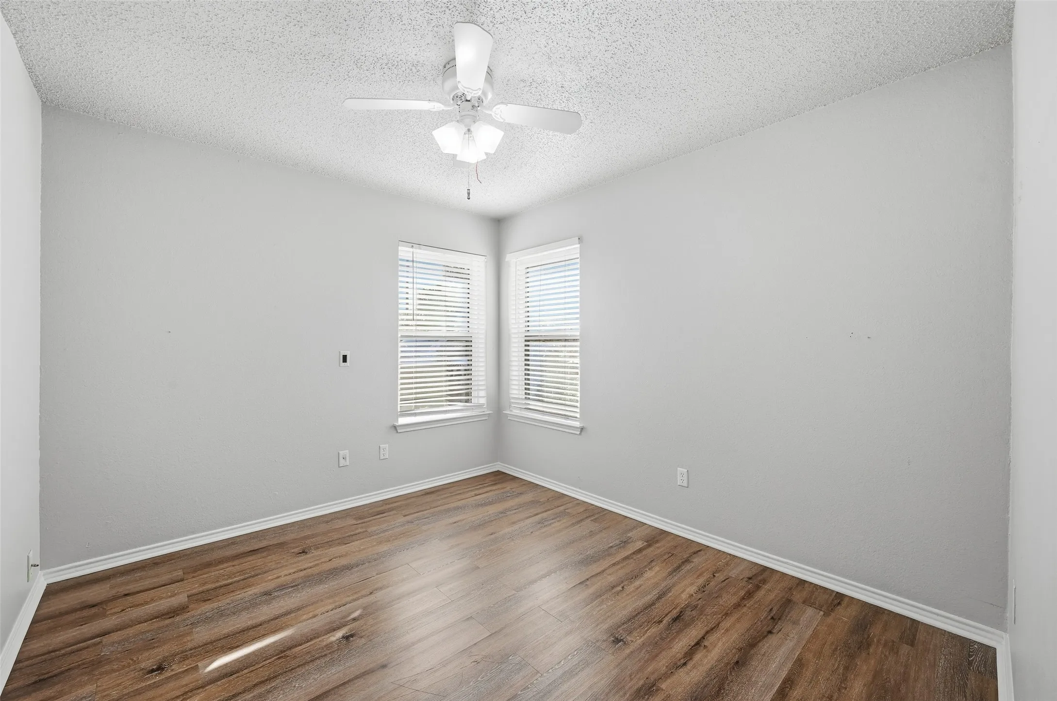 Wood-finish flooring, corner windows with blinds, and a ceiling fan with integrated lighting