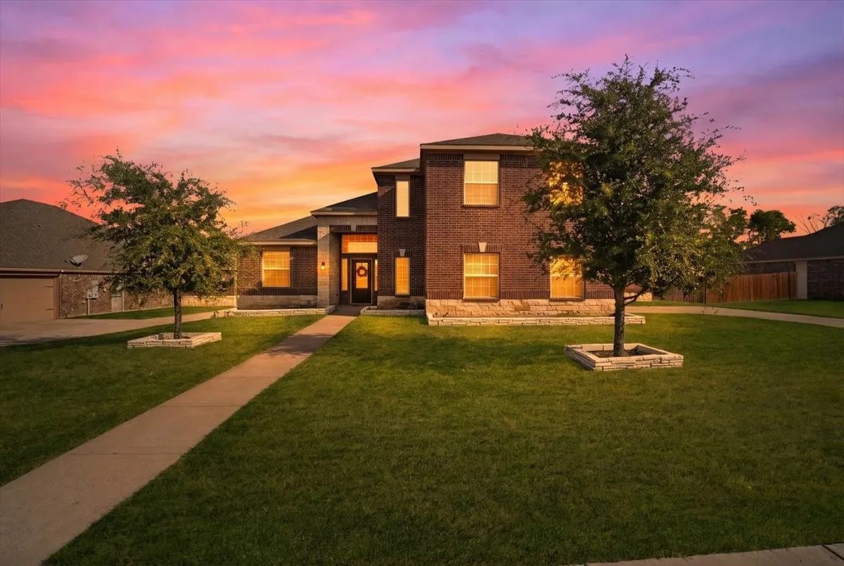 Brick facade with stone accents, covered entry, front yard landscaping, and mature trees