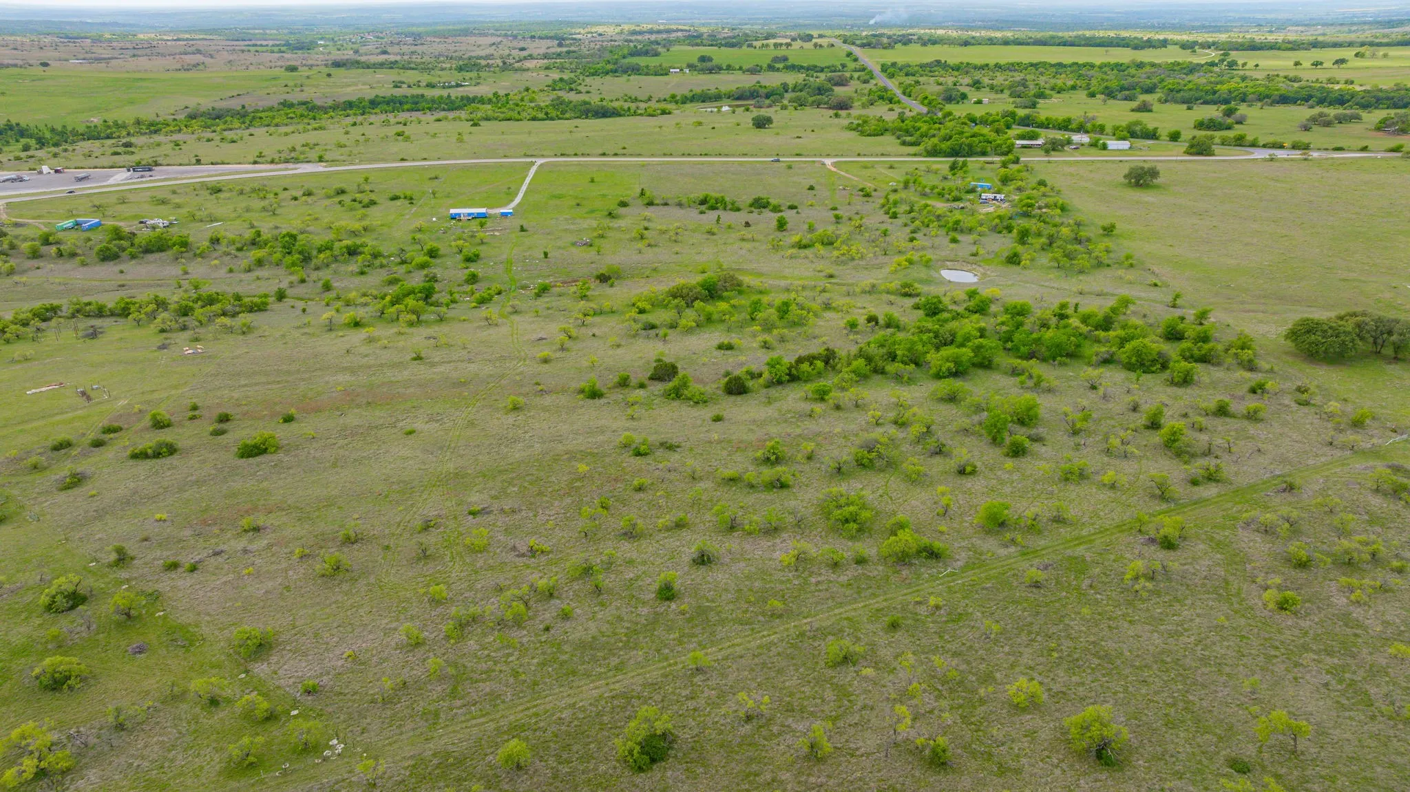 Expansive open landscape featuring green vegetation, scattered trees, and a distant road