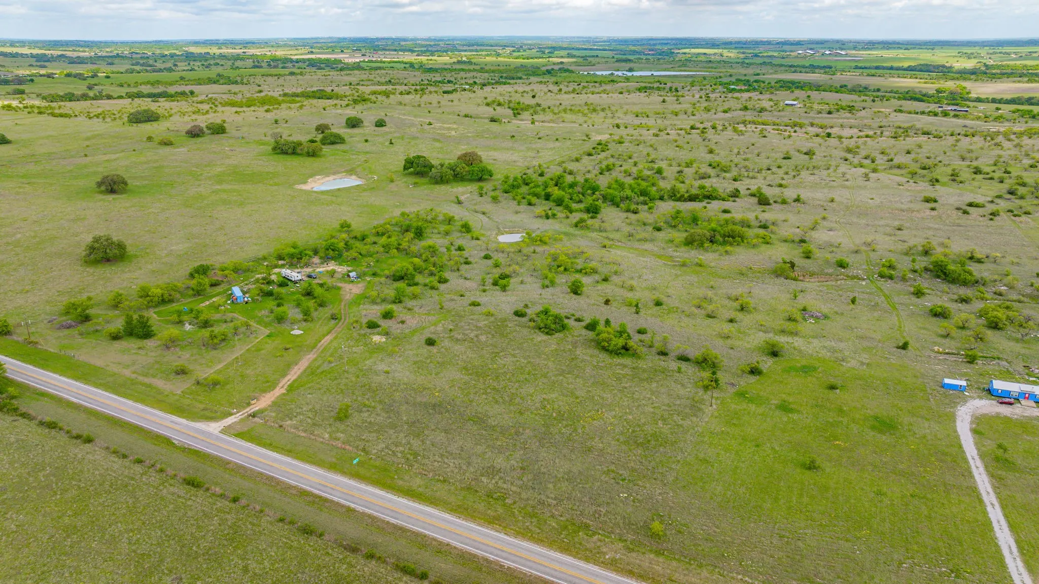 Expansive land featuring a paved road, natural ponds, scattered trees, and open fields