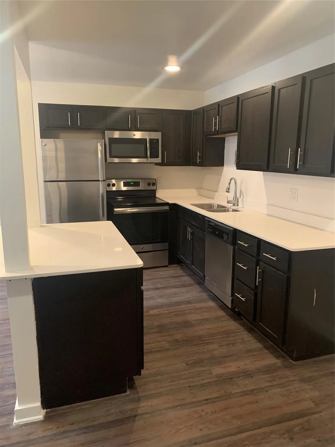L-shaped kitchen with dark wood-finish cabinetry, white countertops, stainless steel appliances, and wood-finish flooring