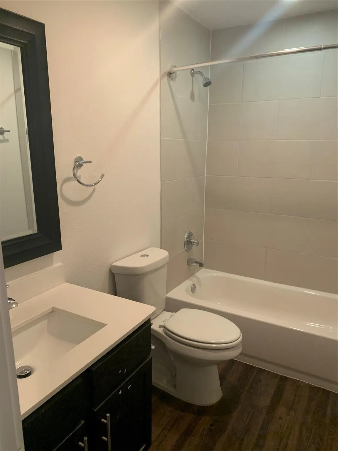 Vanity with integrated sink and storage, wood-finish flooring, tiled shower surround, and bathtub with shower fixture