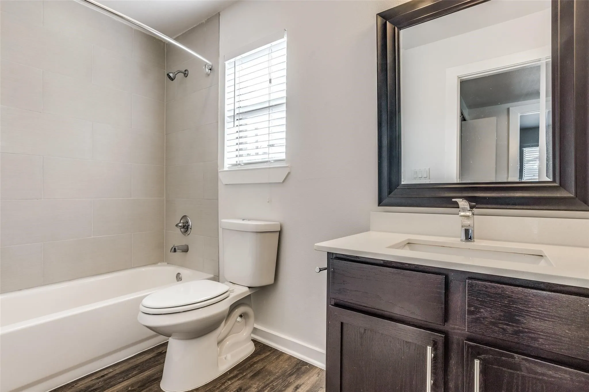 Bathroom featuring a dark wood-finish vanity with a light countertop, a framed mirror, and wood-finish flooring