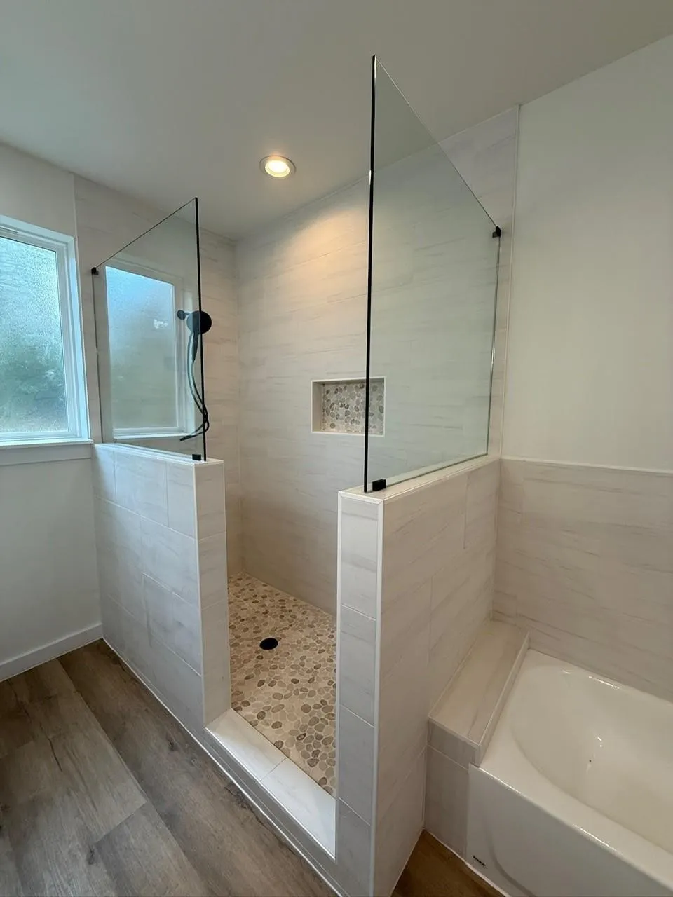 Walk-in shower with pebble tile flooring, built-in niche, and glass panel enclosure