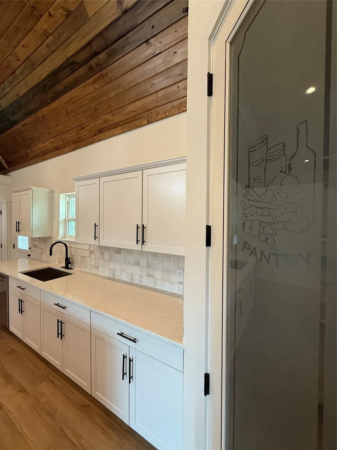 Kitchen featuring white cabinetry, light-toned countertops, a tile backsplash, and wood-finish flooring