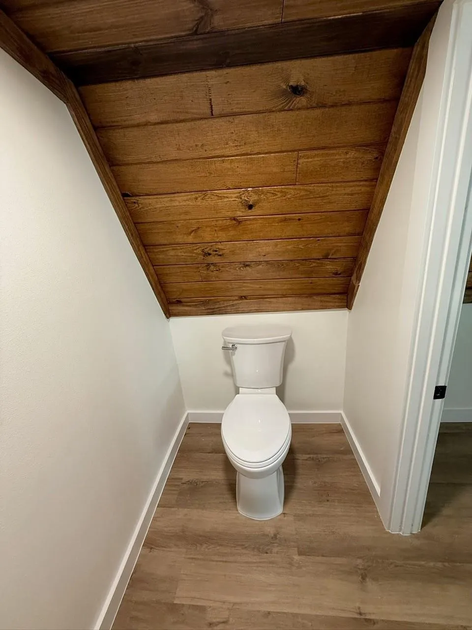 Wood-finish flooring with white baseboards and a white toilet