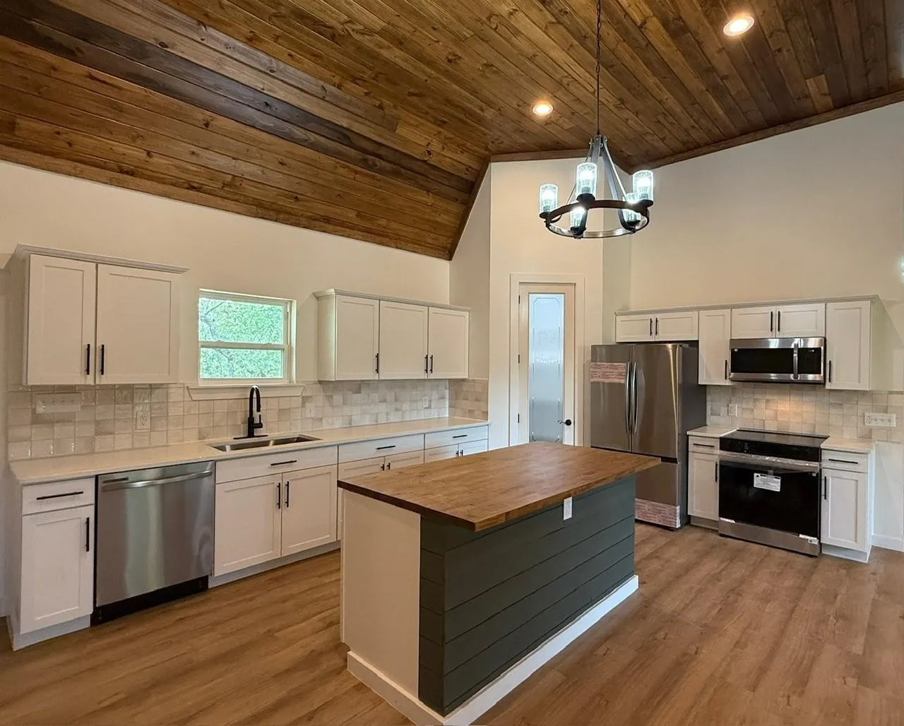 Soaring vaulted ceiling with wood paneling, wood-finish flooring, central island with wood countertop, white cabinetry with dark hardware, and stainless steel appliances