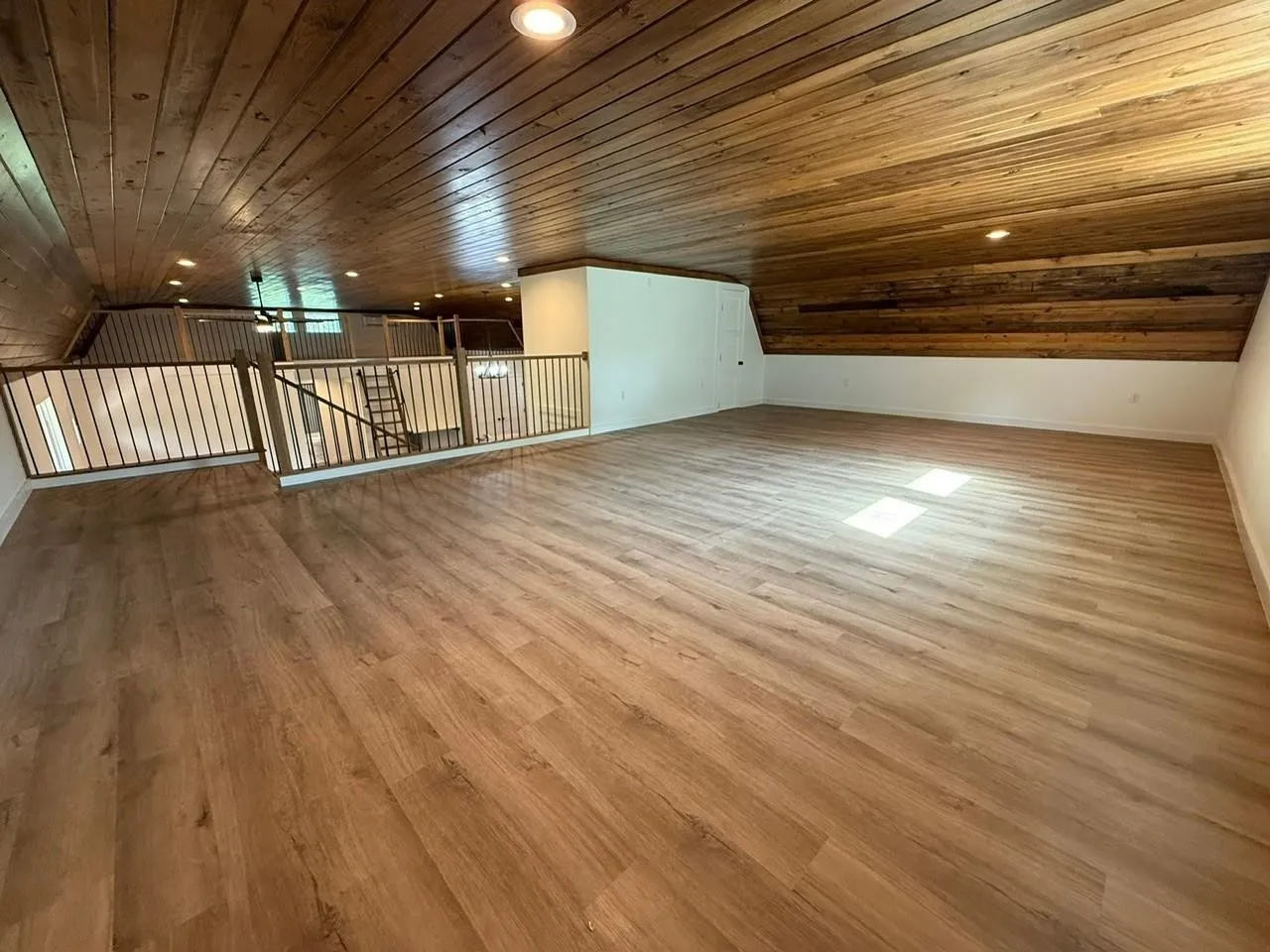 Spacious loft area featuring wood-finish flooring, a wood-paneled ceiling, recessed lighting, and a metal railing