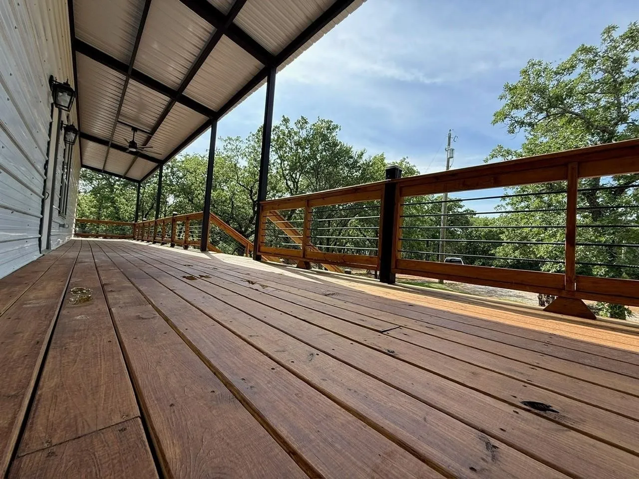 Expansive wood deck with metal cable railing and a corrugated metal roof
