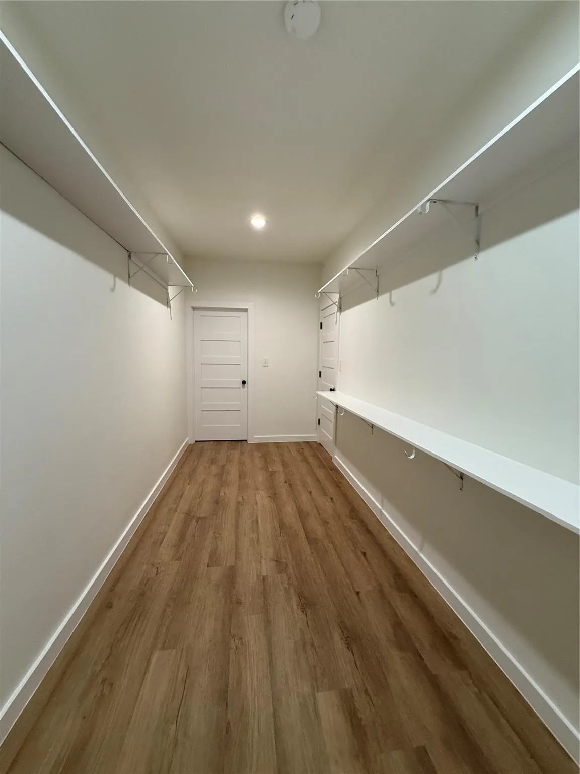 Recessed lighting illuminates the wood-finish flooring in this space featuring built-in shelving, a full-lite door, and white trim