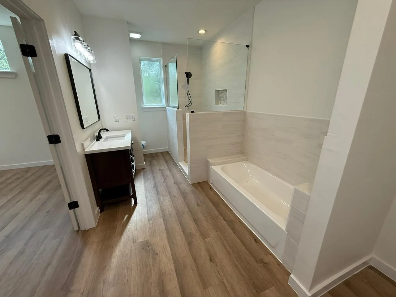 Wood-finish flooring, white walls, dark wood vanity with white countertop, recessed lighting, and a walk-in shower with glass enclosure