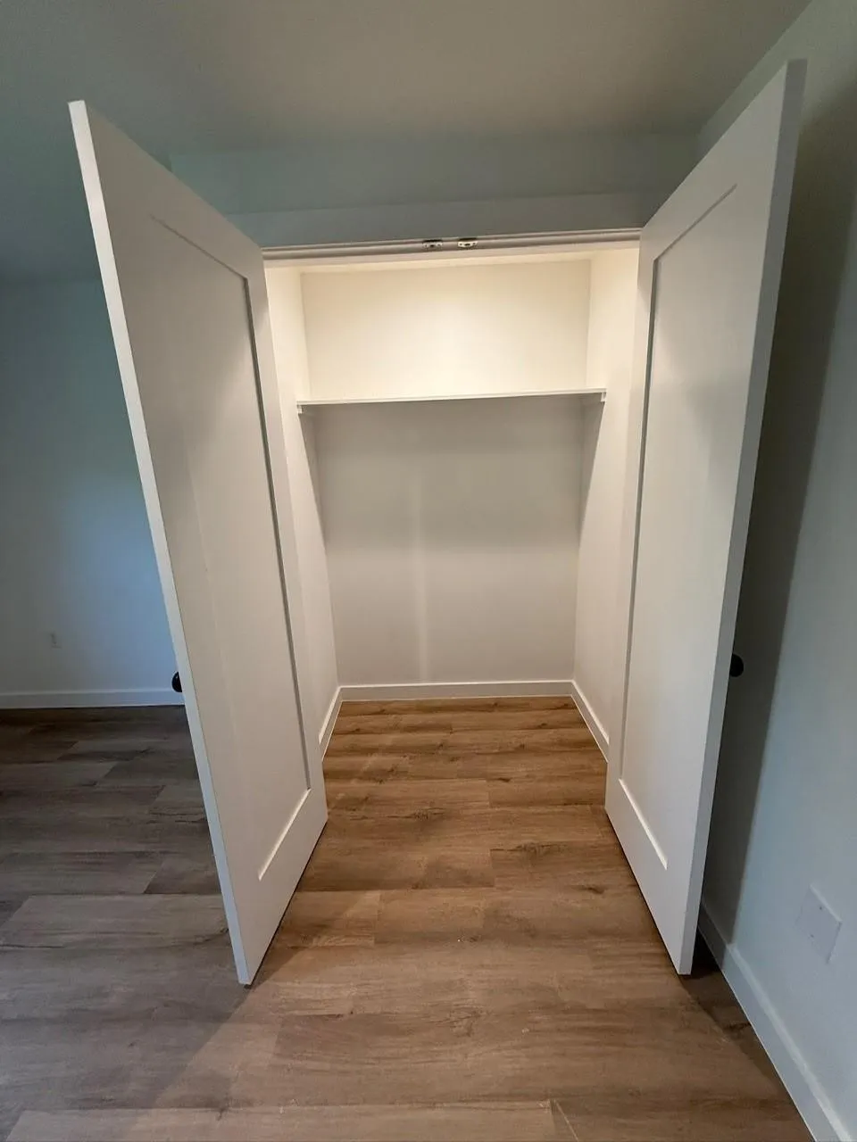 Built-in closet with double white shaker doors, integrated shelving, and a hanging rod, complemented by wood-finish flooring