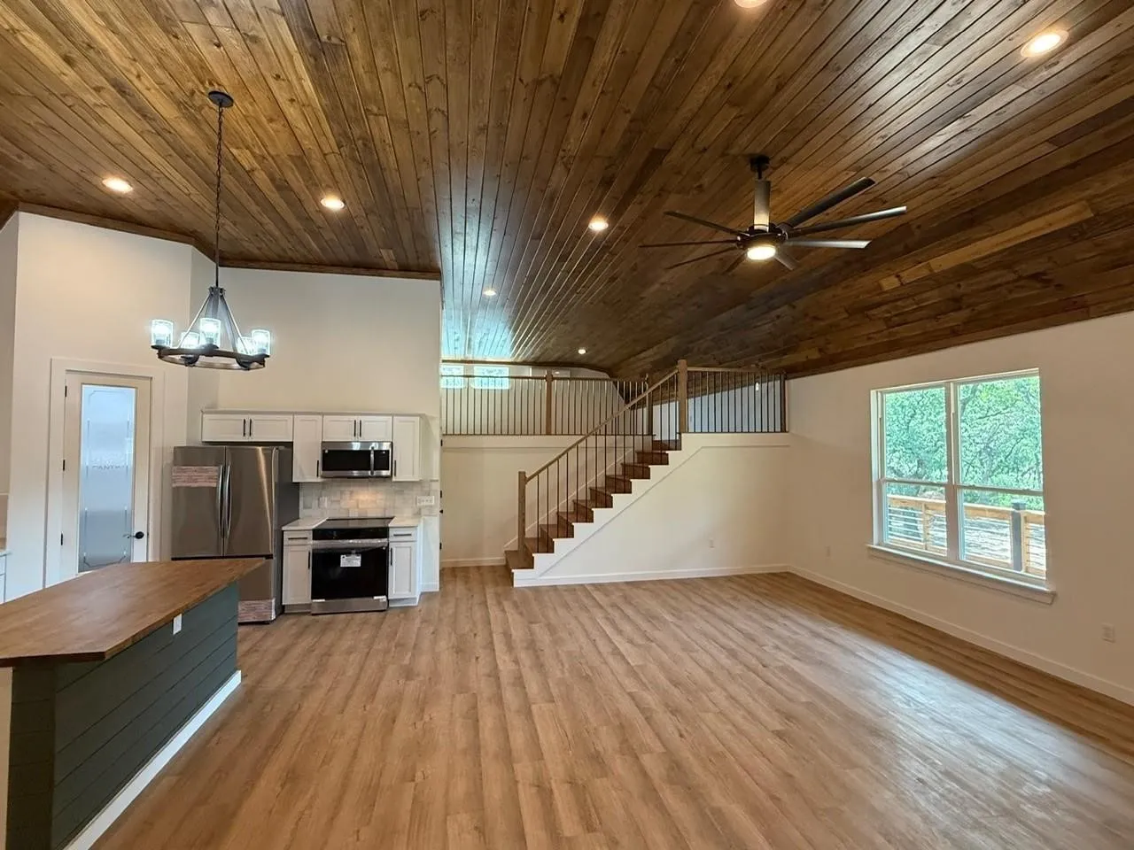Vaulted wood-plank ceiling, wood-finish flooring, white kitchen cabinetry with stainless steel appliances, and a wood-top kitchen island