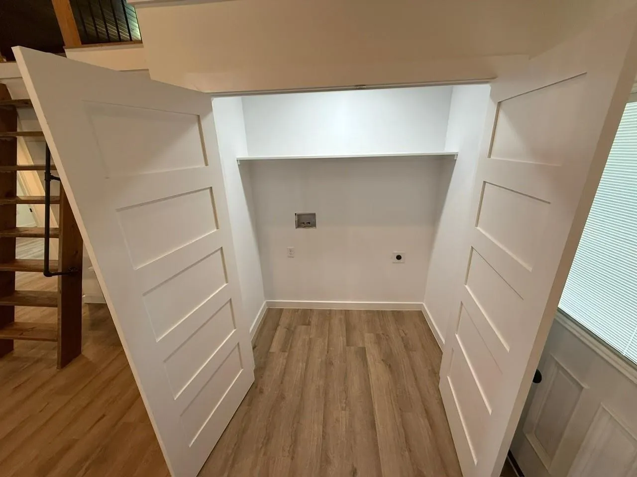 Utility closet with wood-finish flooring, white paneled doors, and an upper shelf