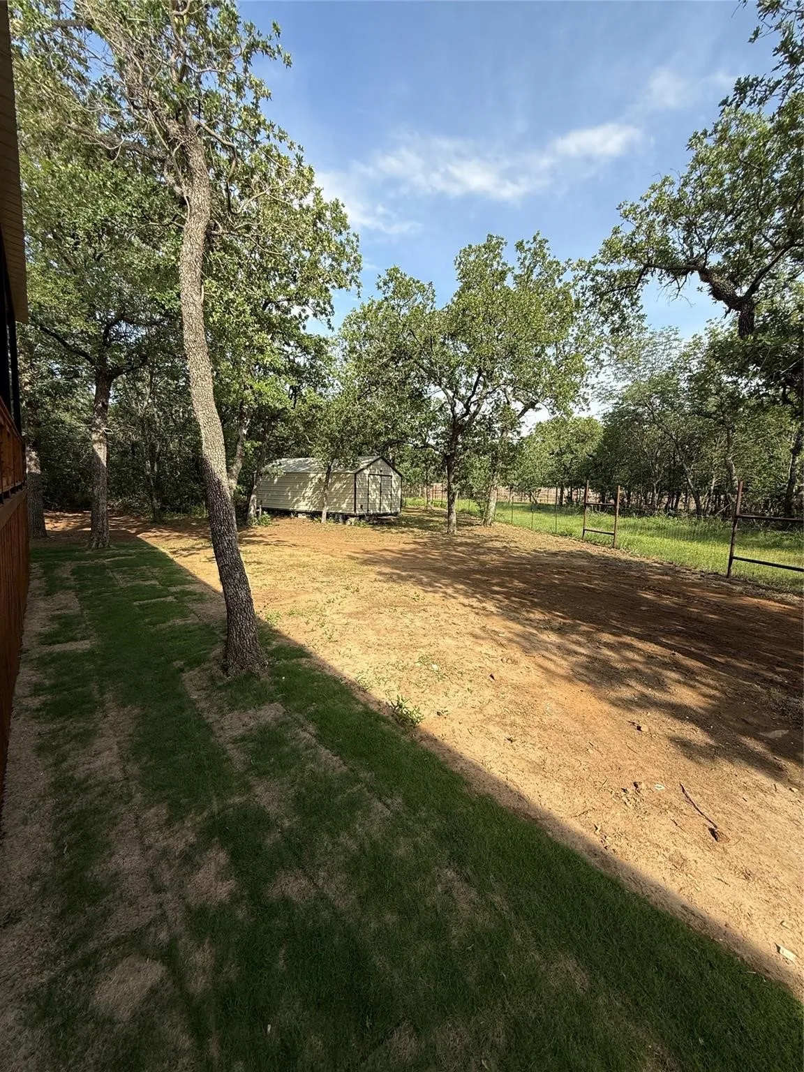 Expansive outdoor space featuring established trees, a utility shed, and partial fencing