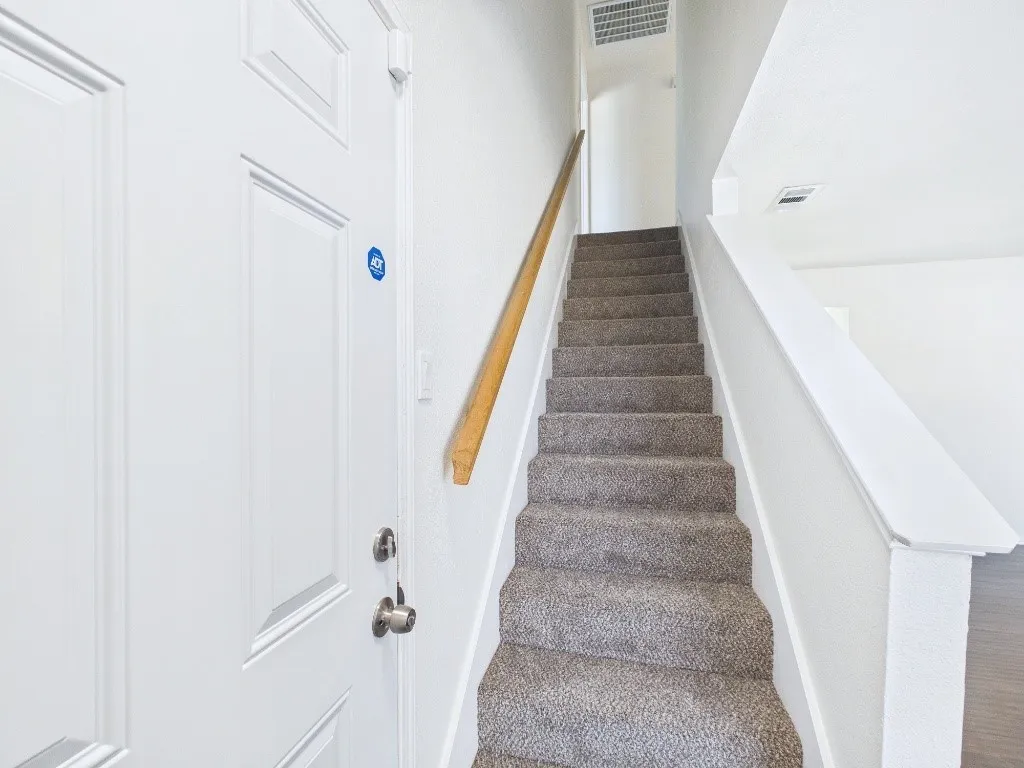 Carpeted stairway with a natural wood-finish handrail and painted white balustrade