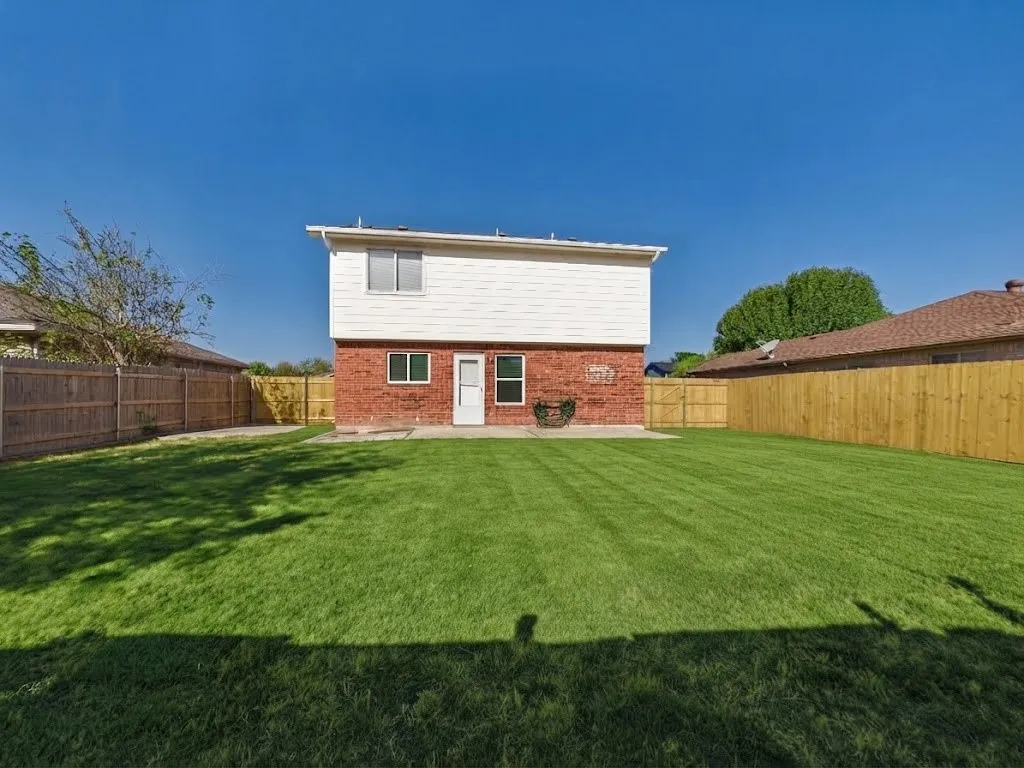 Expansive backyard featuring a manicured lawn, full privacy fencing, and a concrete patio pad
