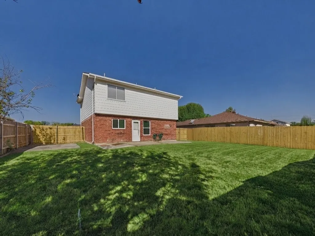 Expansive lawn area with a new wooden privacy fence, a concrete patio, and a two-story exterior featuring brick and white siding