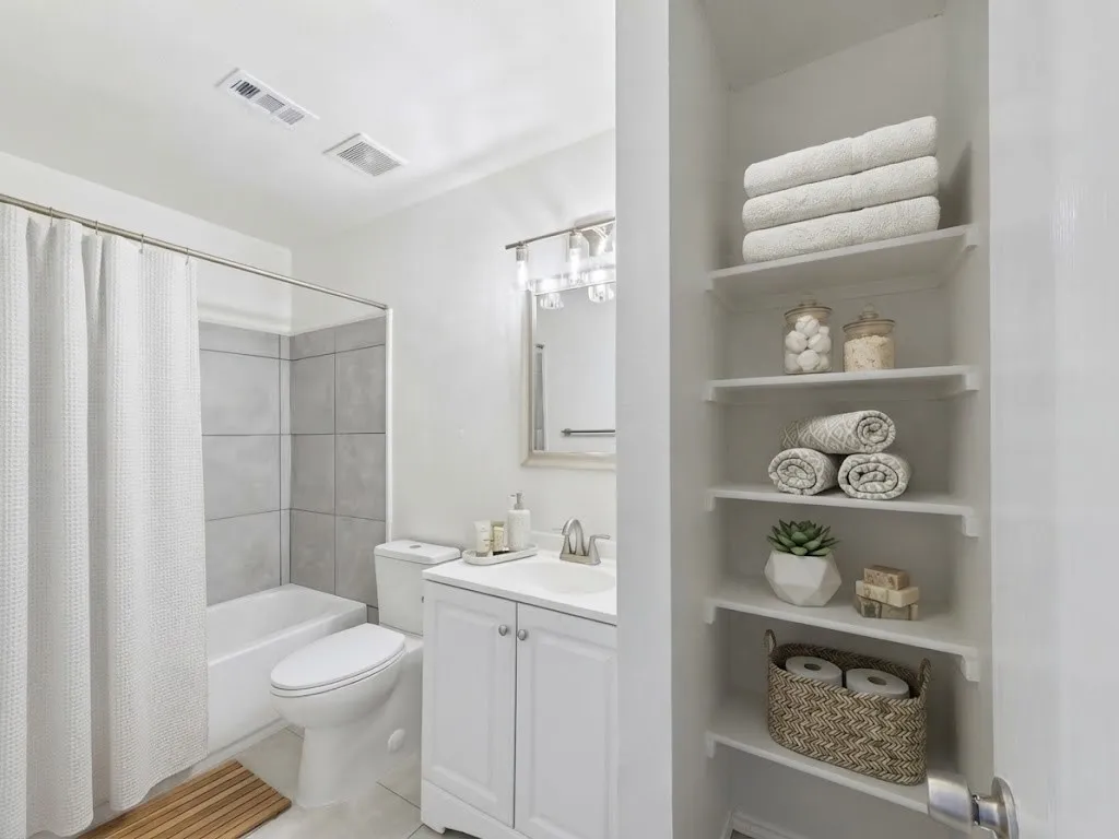 Built-in shelving, white vanity with dual-door cabinetry, tub/shower combination with tile surround, wall-mounted light fixture, and a framed mirror