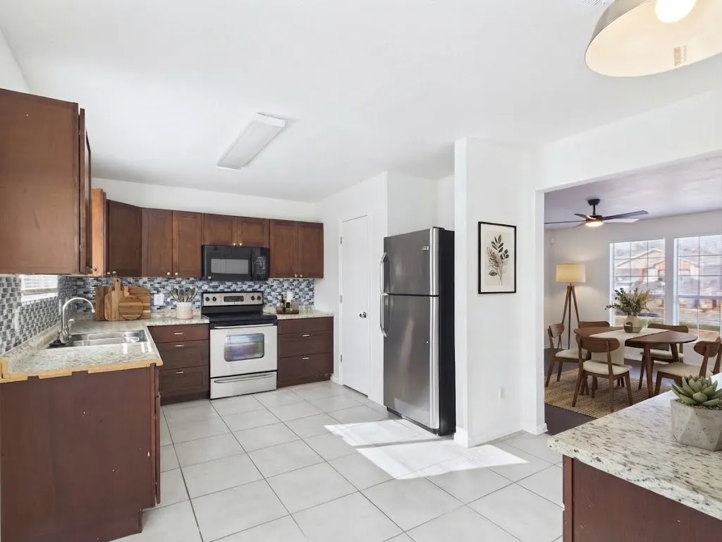 Kitchen featuring wood cabinetry, stainless steel appliances, mosaic tile backsplash, and light-toned tile flooring