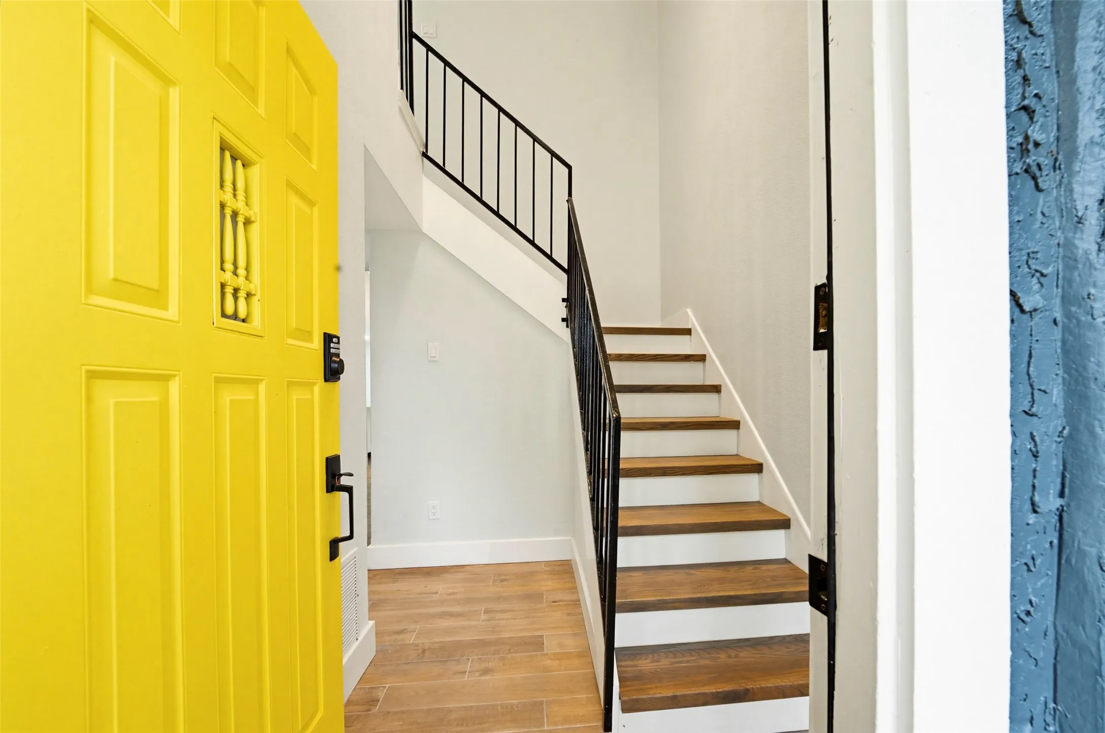 Entryway featuring a bright paneled door with window detail, wood-finish flooring, and a staircase with a black metal railing