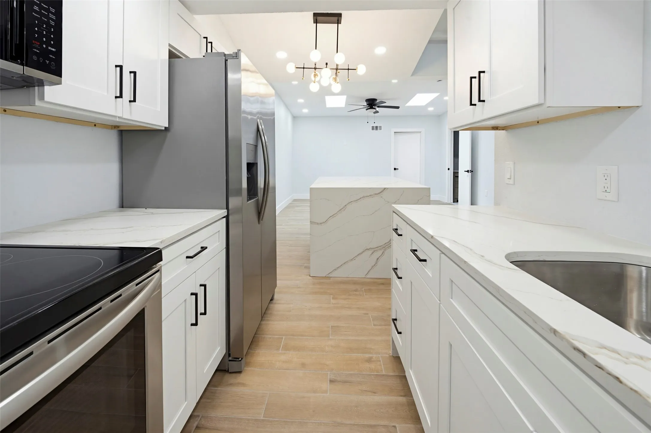 Kitchen featuring white shaker cabinetry, stainless steel appliances, wood-finish flooring, white countertops, and a modern chandelier