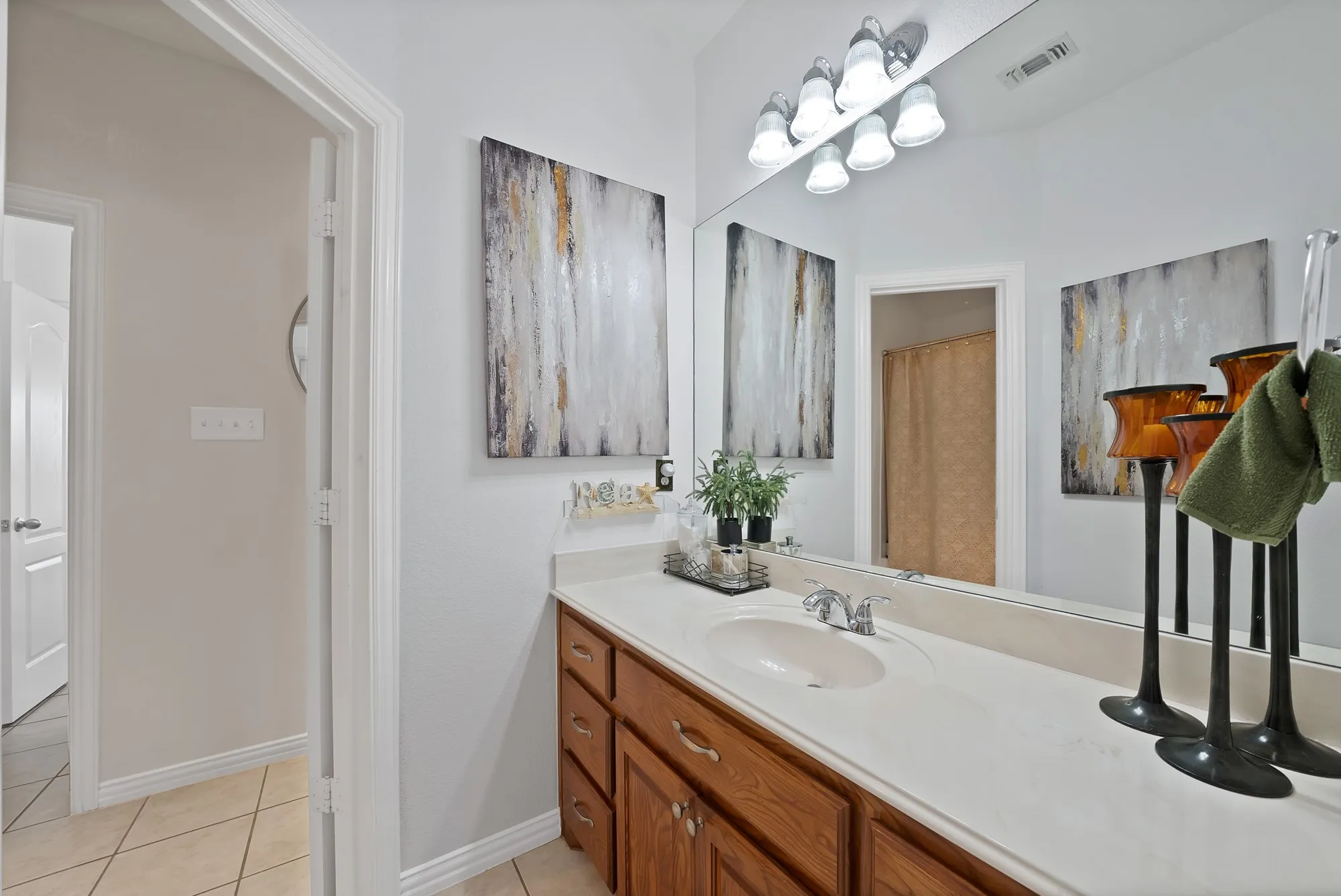 Secondary bathroom, upper level — Single-sink vanity with oak cabinetry and white countertop, full-width mirror, multi-bulb vanity bar light, tile flooring, and separate water closet with tub-shower combination visible through door.