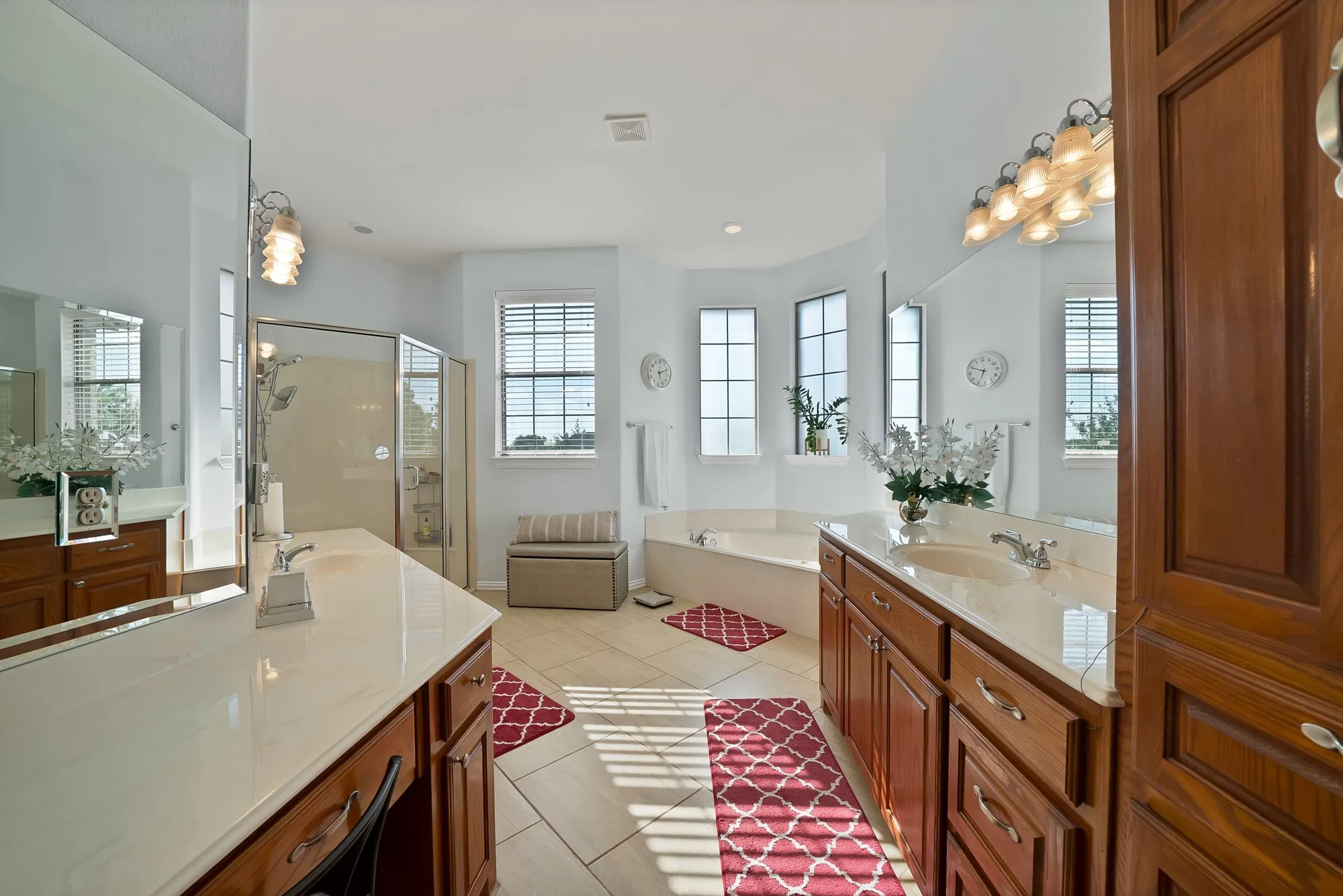 Primary bathroom, second angle — Frameless glass walk-in shower with full-surround tile, garden tub with tile deck surround, dual oak vanities with white quartz countertops, large-format tile flooring, and five-window bank providing natural light on three walls.