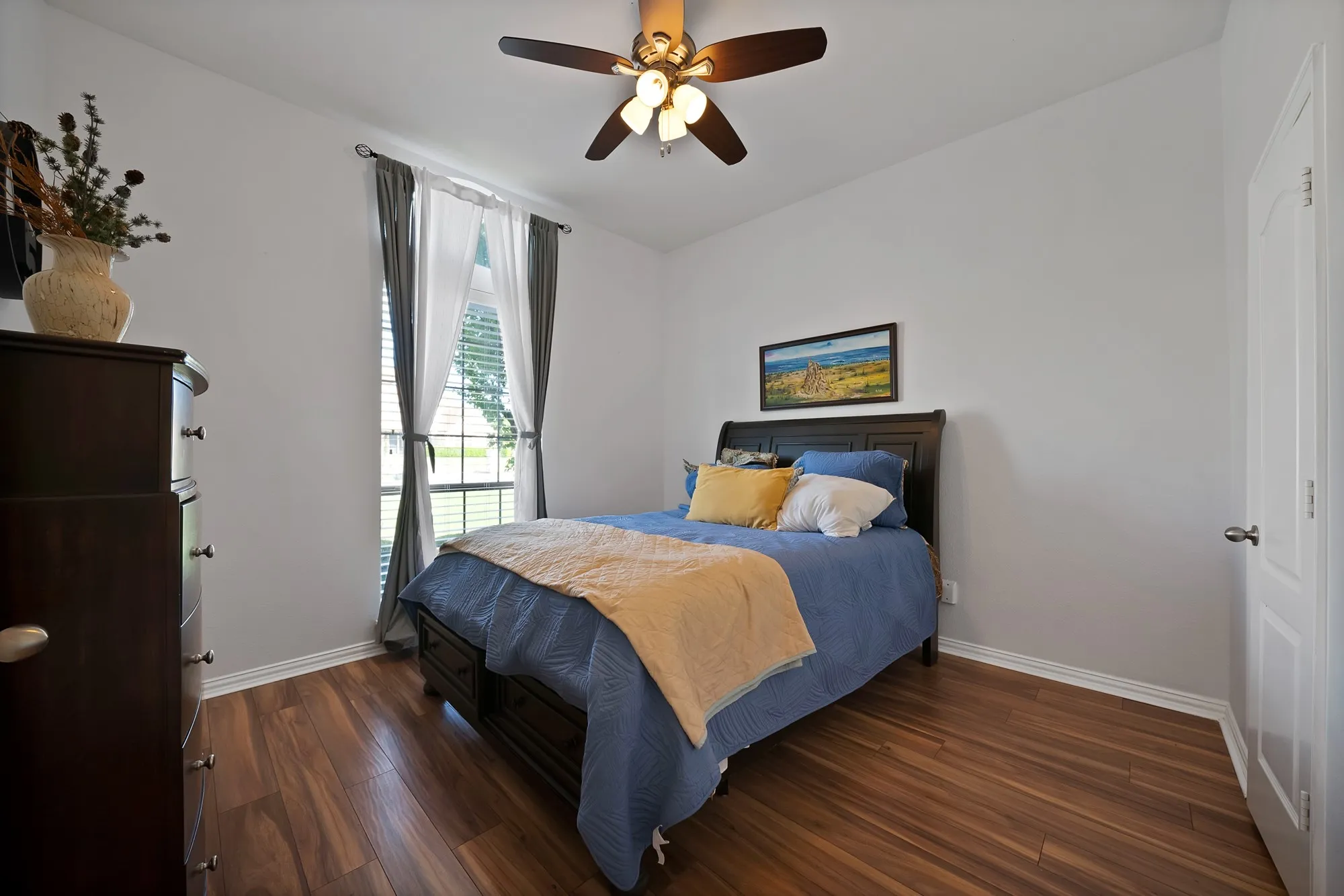 Secondary bedroom — Dark hardwood floors, ceiling fan with light kit, double windows with drape rod, and standard closet door. Room accommodates full or queen bed.