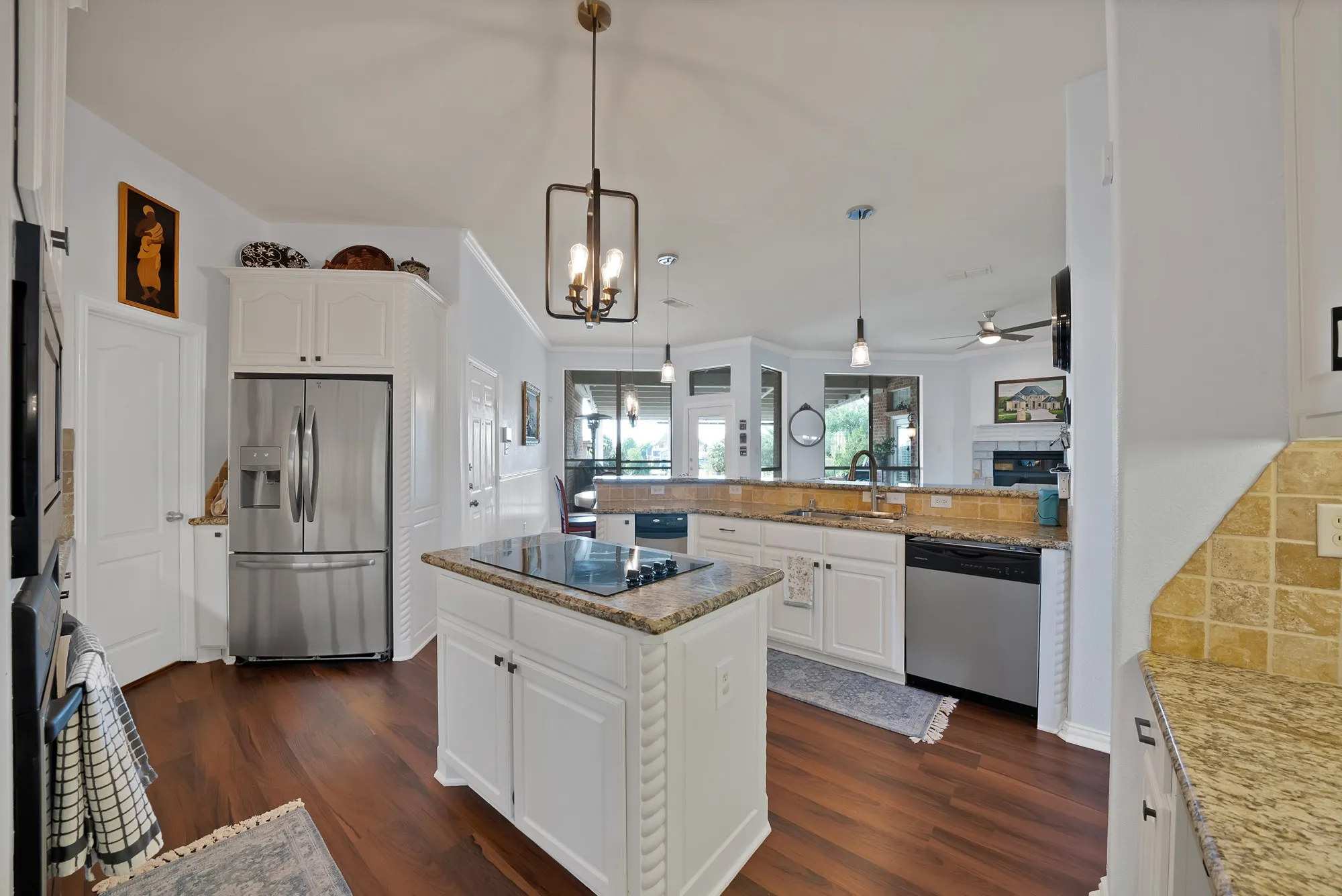 Kitchen, second angle — Stainless French door refrigerator, built-in microwave, double wall oven, center island with cooktop and granite countertop, and stainless dishwasher. White cabinetry extends to ceiling height with upper storage.