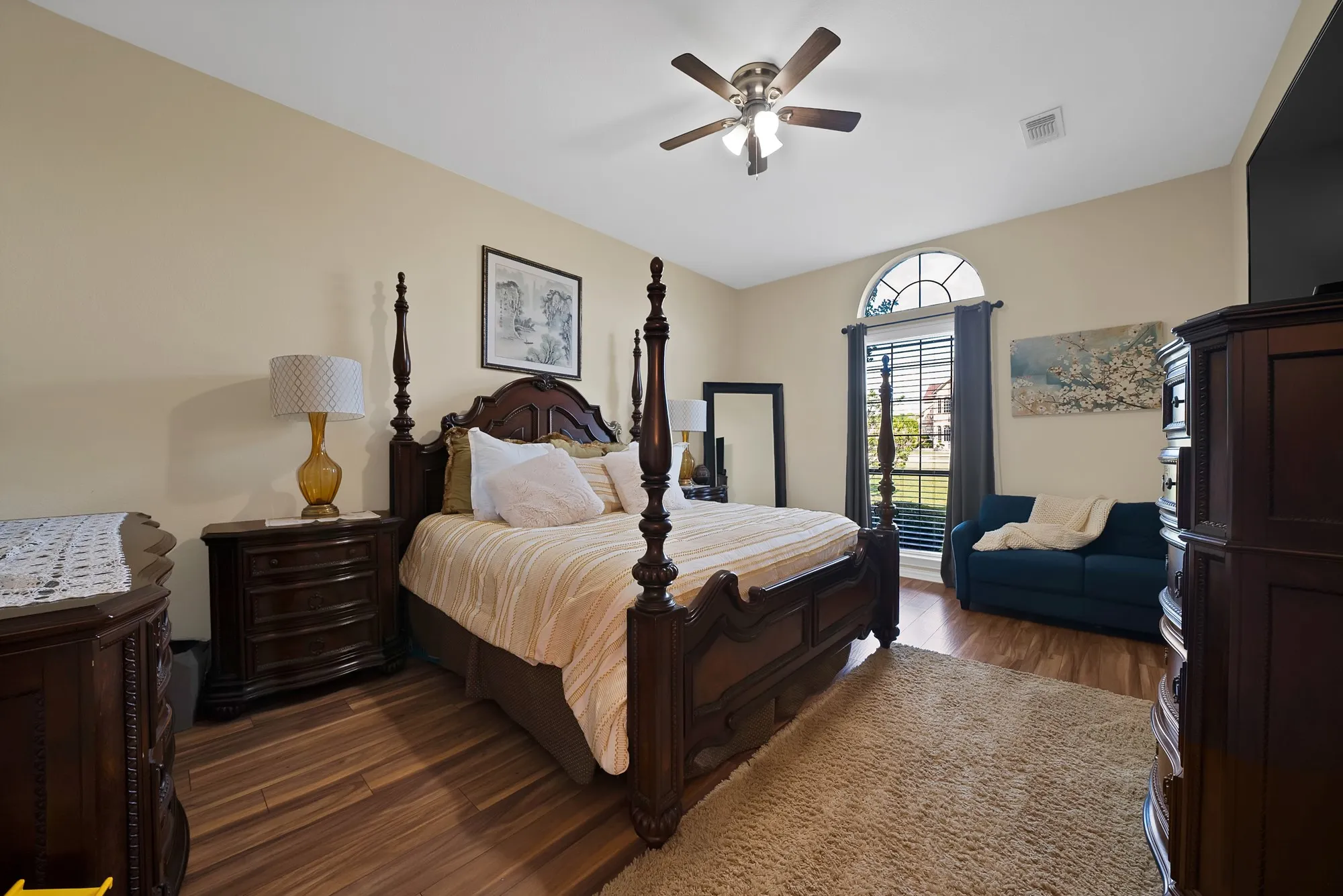 Secondary bedroom, upper level — Dark hardwood floors, ceiling fan with light kit, arched transom window, and room size accommodating a queen or king bed with sitting area.