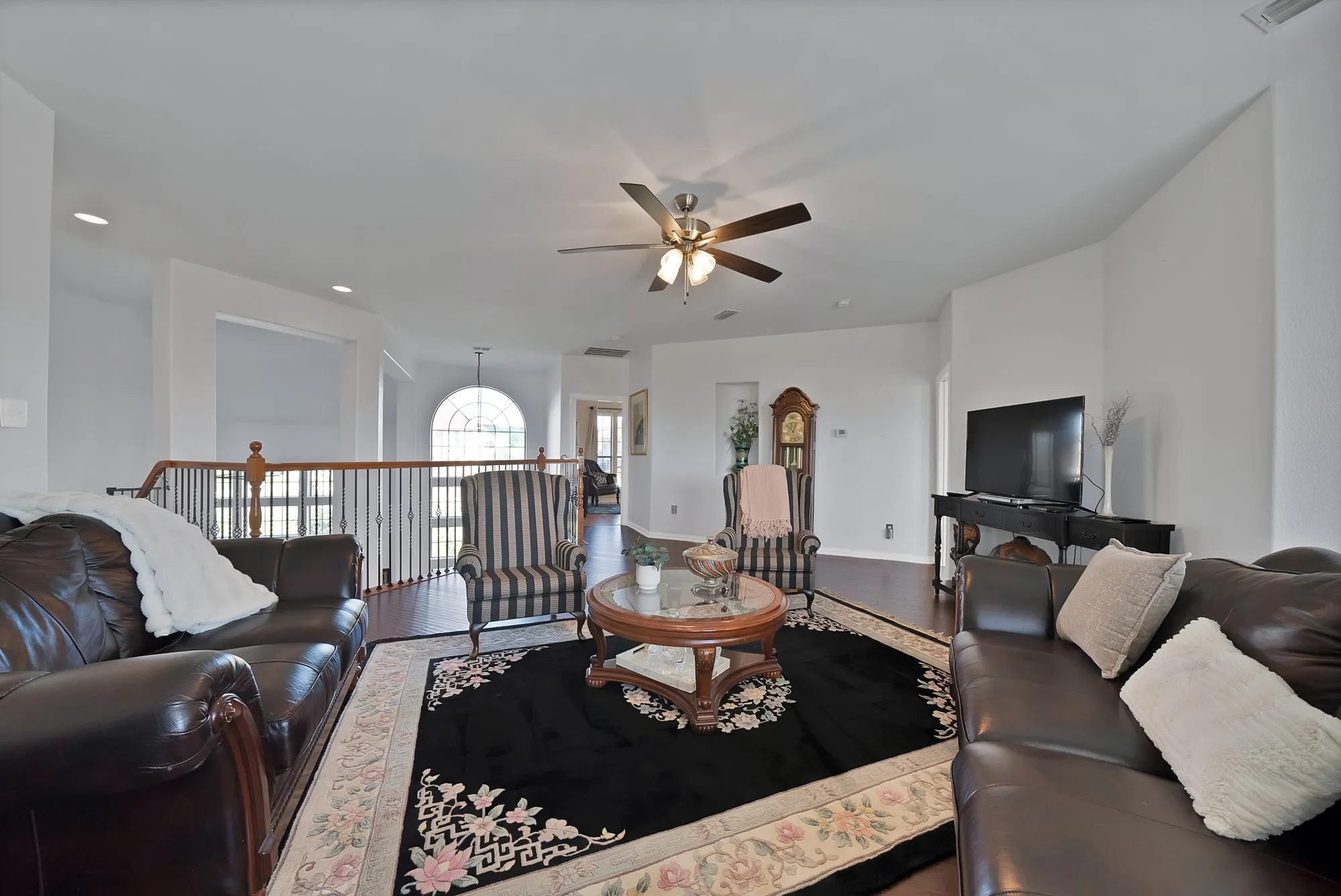 Upper-level living area, second angle — Dark hardwood floors, ceiling fan, French door access to rear balcony, and staircase with decorative wrought iron balusters and wood handrail visible from this angle.