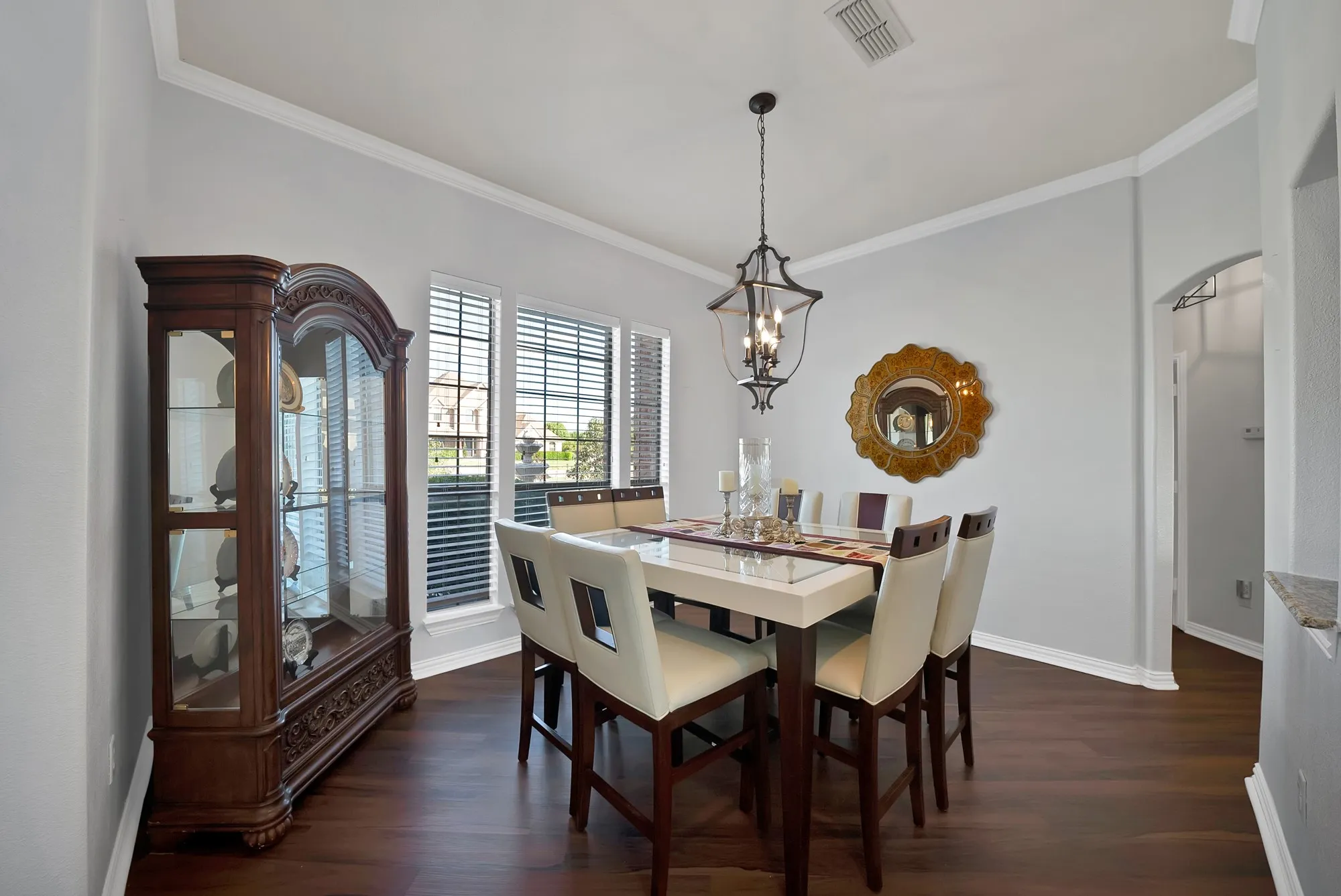 Formal dining room — Tray ceiling with crown molding, dark hardwood floors, iron and glass lantern pendant, and plantation shutters on dual windows.
