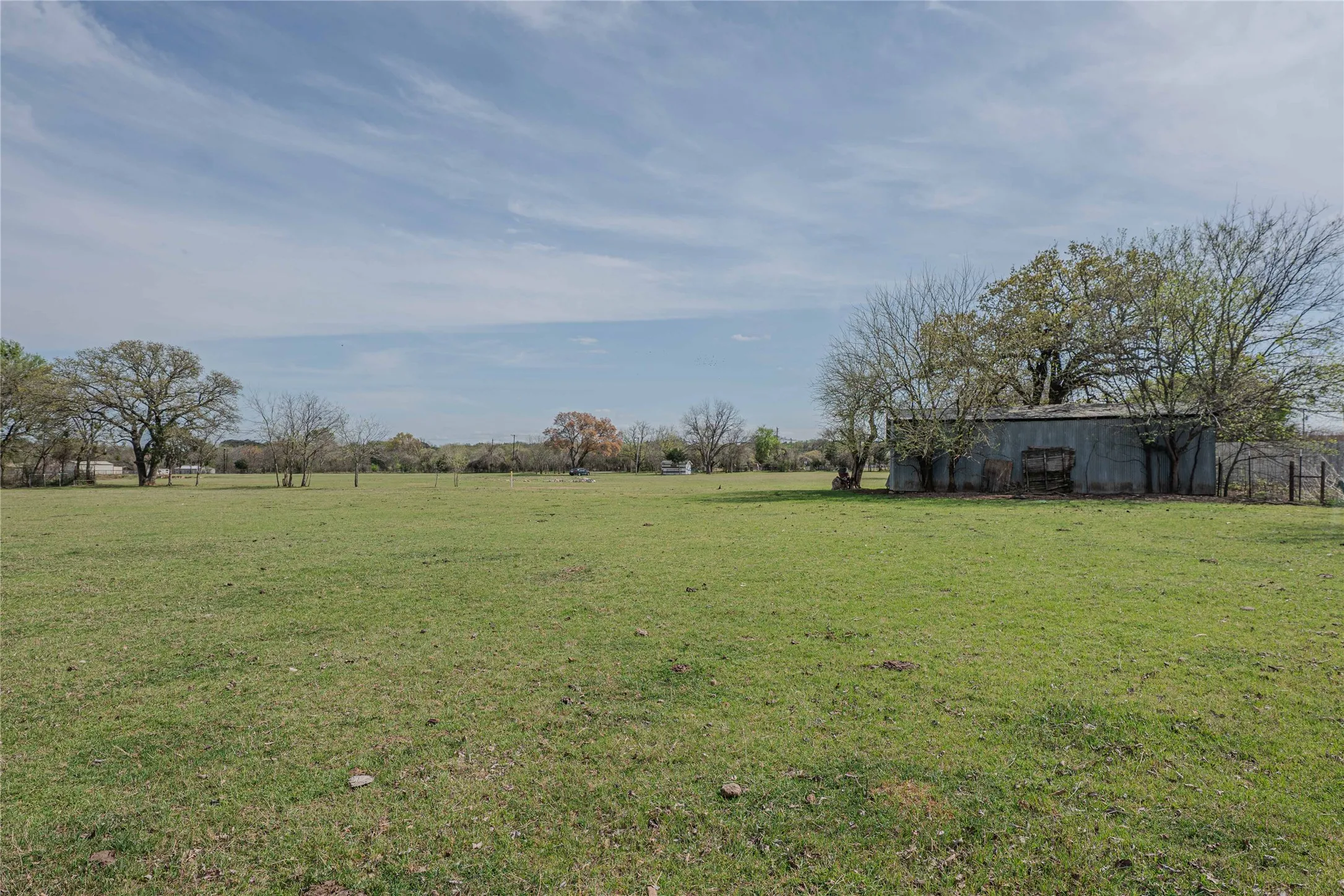 Expansive green field with a metal-clad outbuilding and mature trees