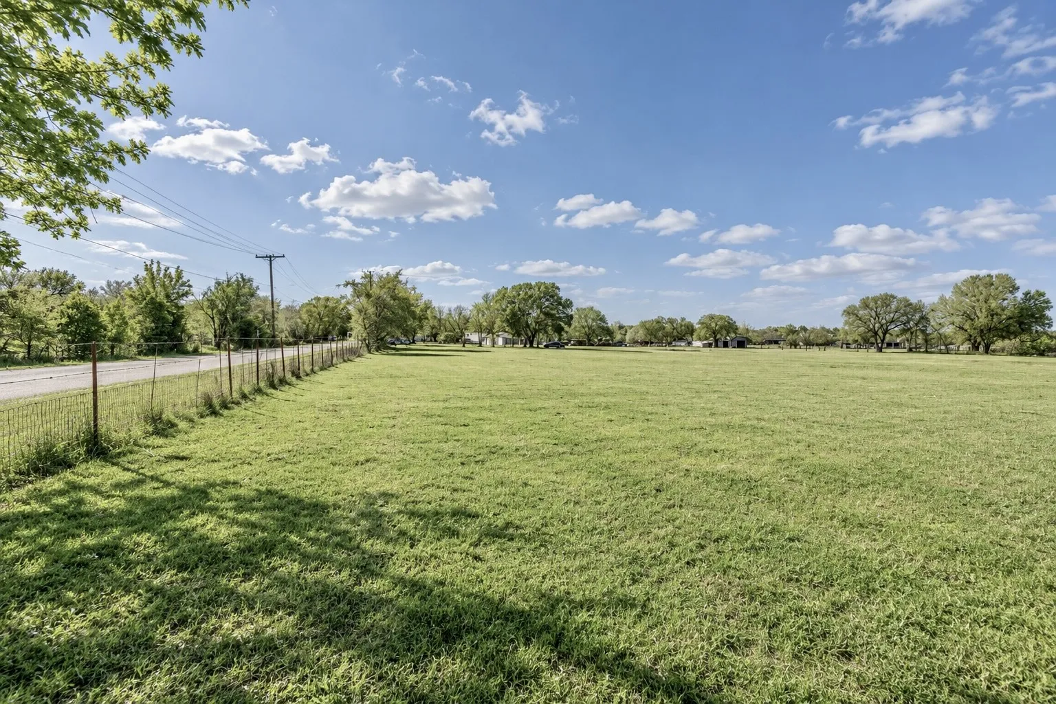 Expansive grassy field with a wire fence lining a paved road