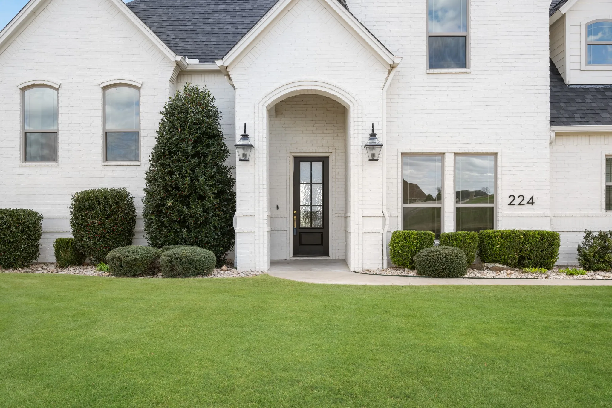 White brick exterior with dark trim windows, arched entry, black paneled front door, and manicured landscaping