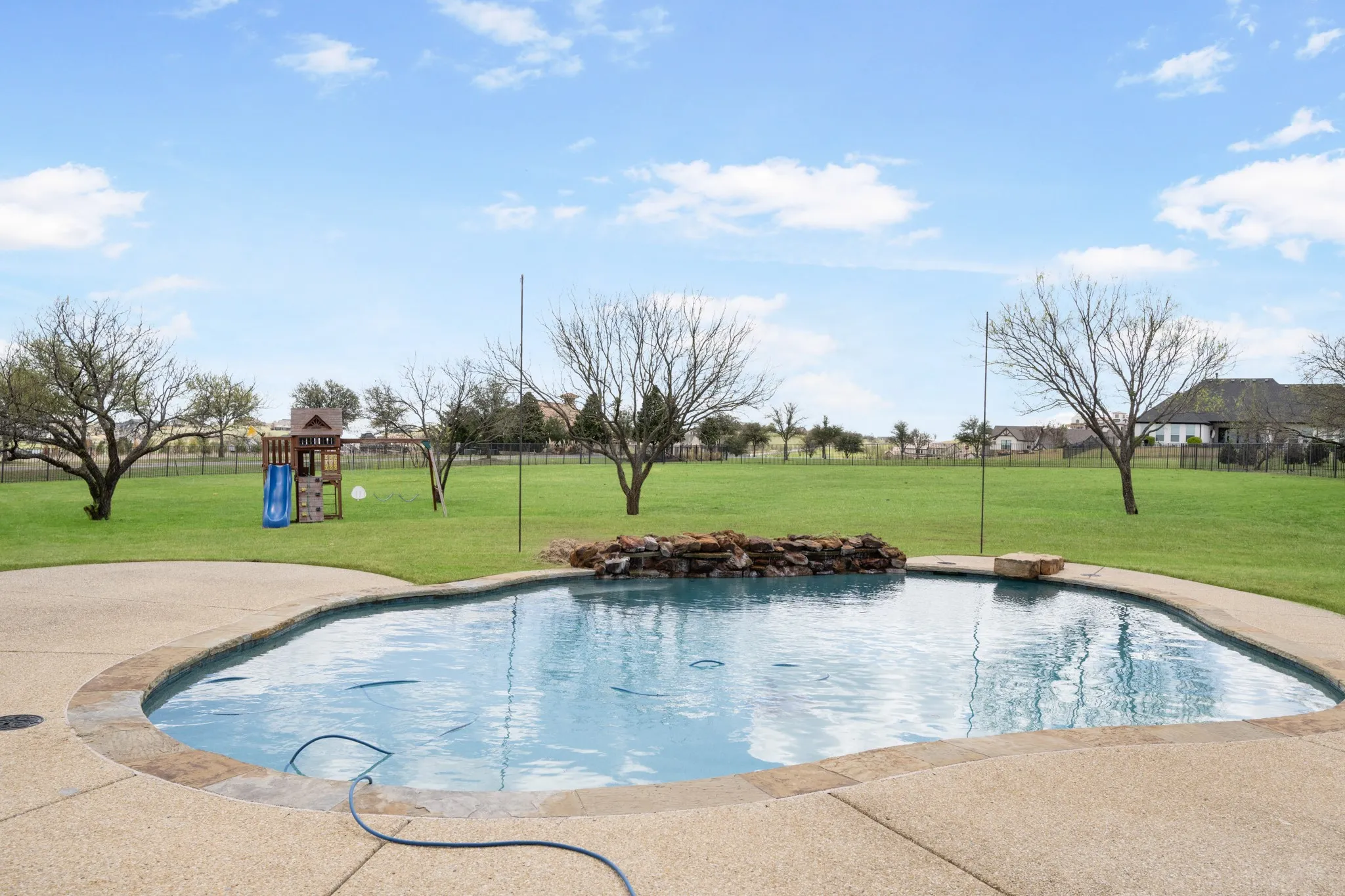 Freeform swimming pool with stone coping, textured concrete decking, and a rock waterfall feature