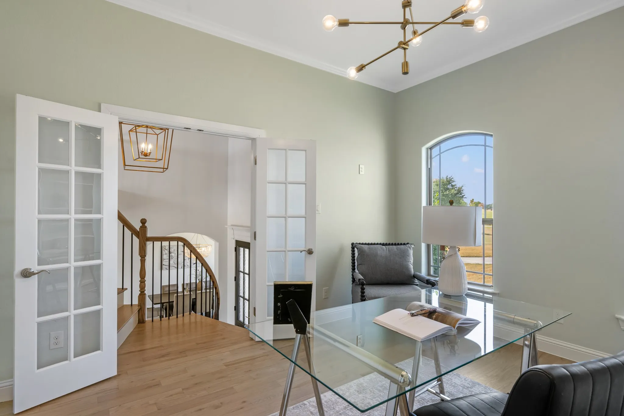French doors with glass panels, light wood-finish flooring, a contemporary chandelier, an arched window, and crown molding