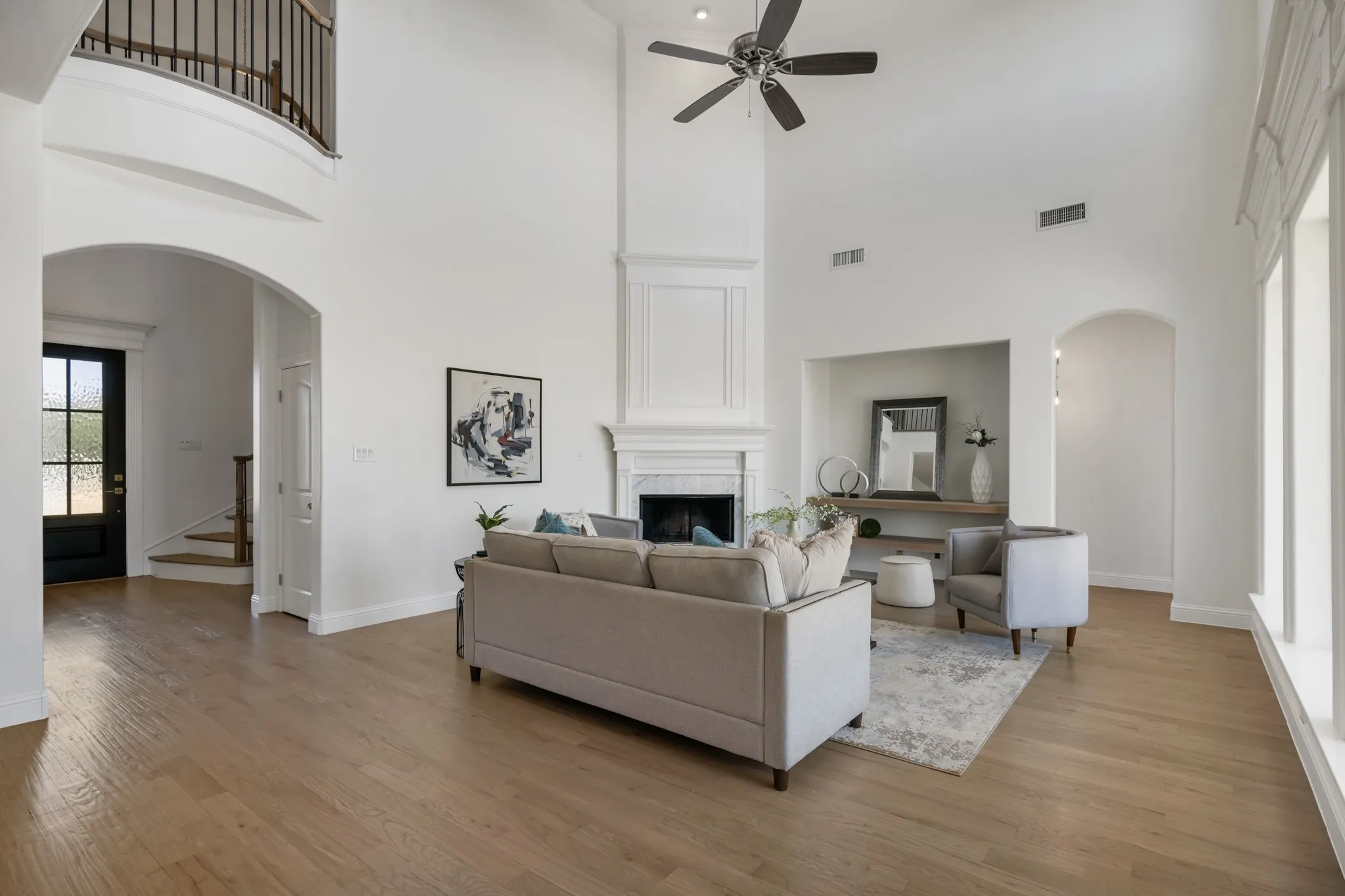 Soaring ceilings with a ceiling fan, light wood-finish flooring, and a fireplace with a mantel