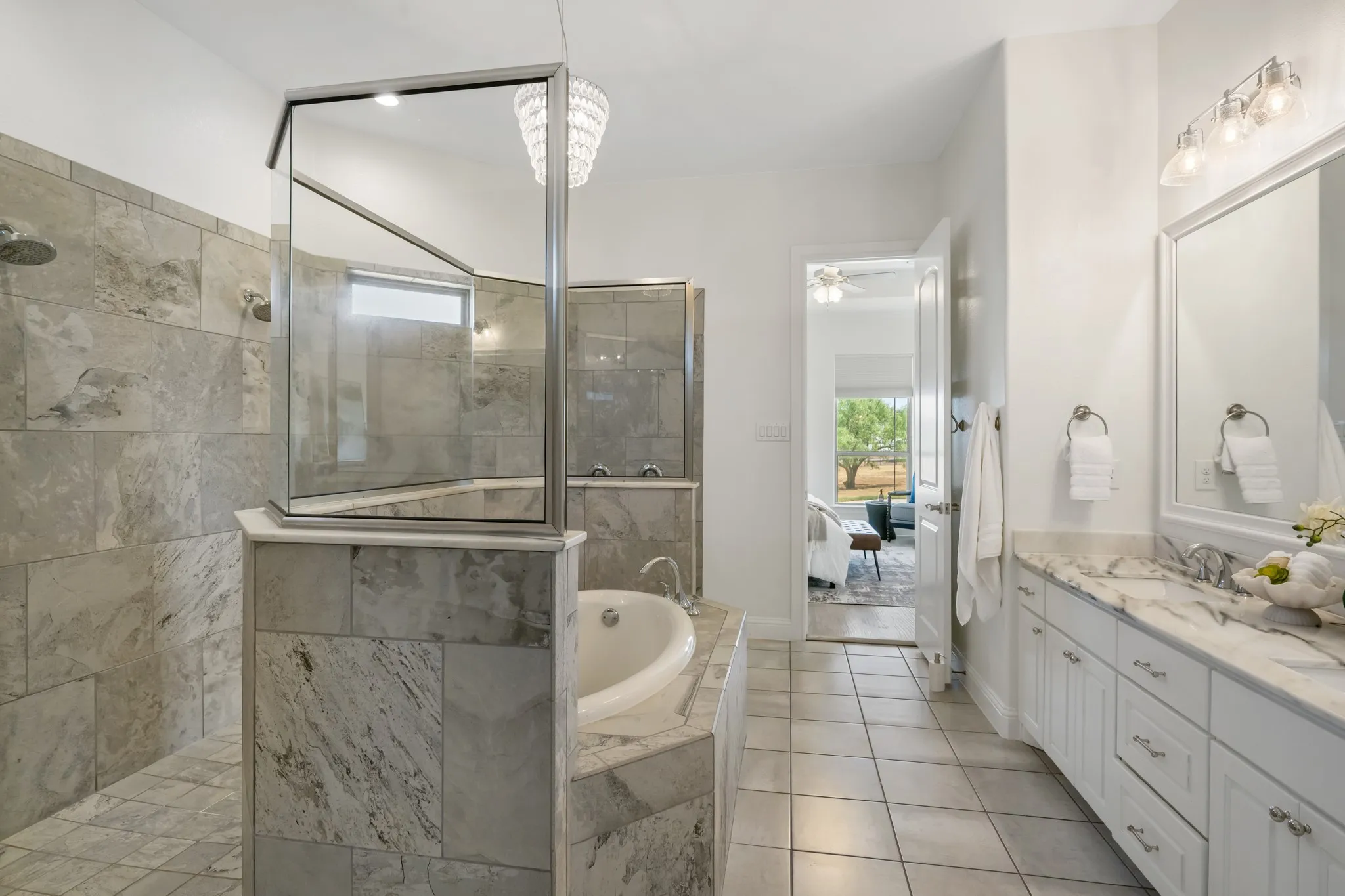 Dual vanity with white cabinetry and stone countertops, large soaking tub, tiled shower with glass enclosure, tiled flooring