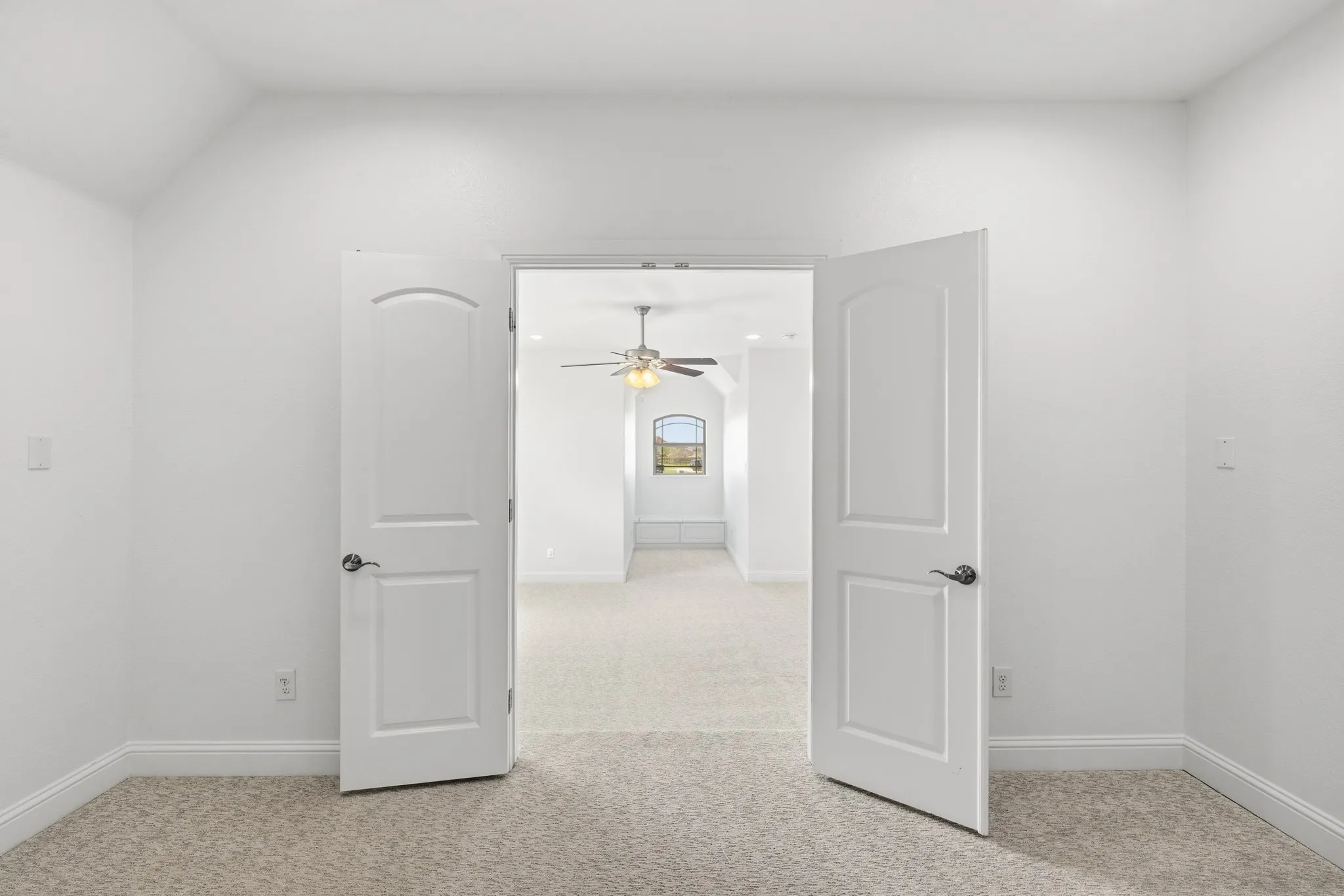Double panel doors opening into a carpeted room with a ceiling fan