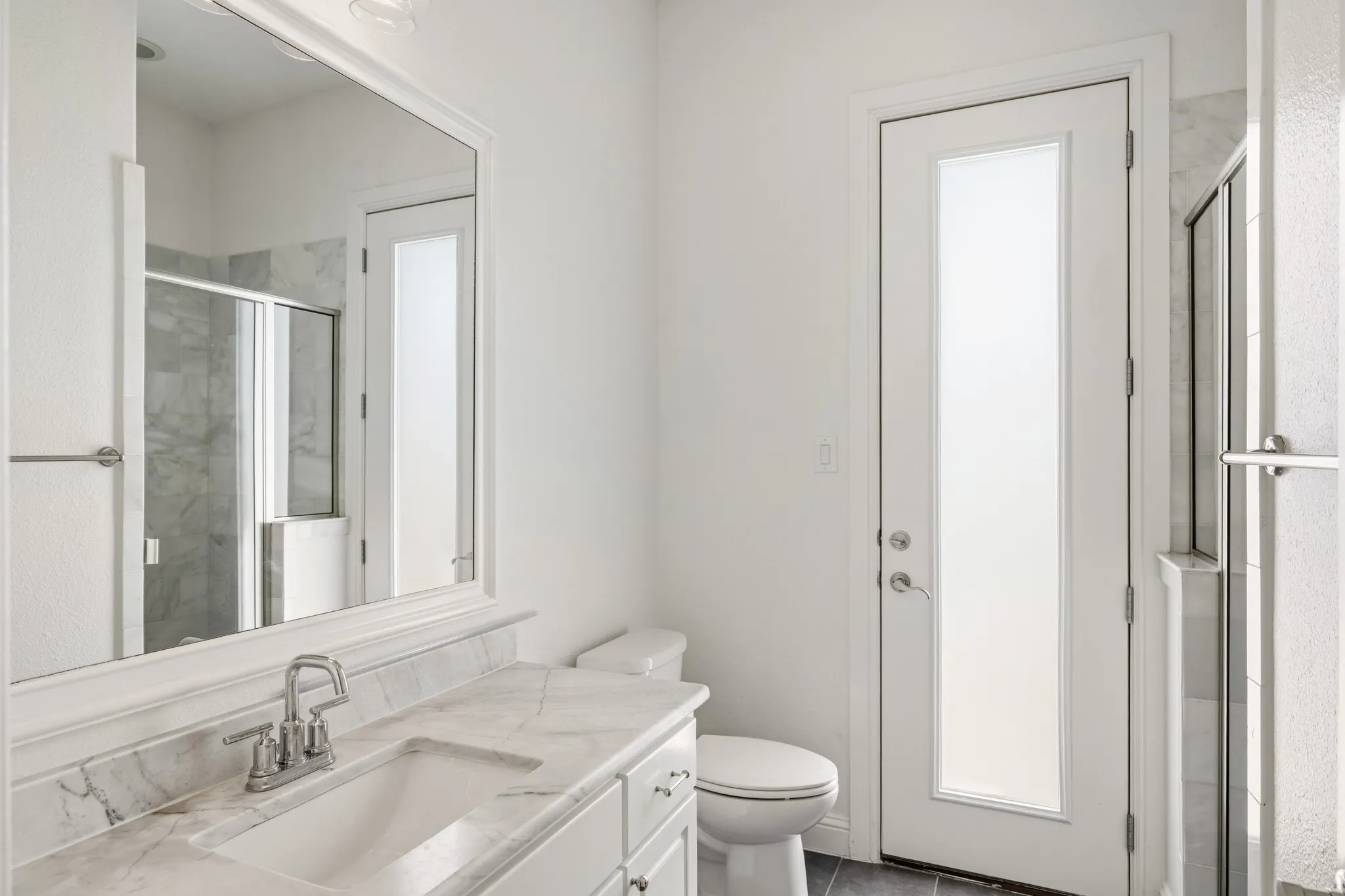 White vanity with a stone countertop, chrome fixtures, and a framed mirror