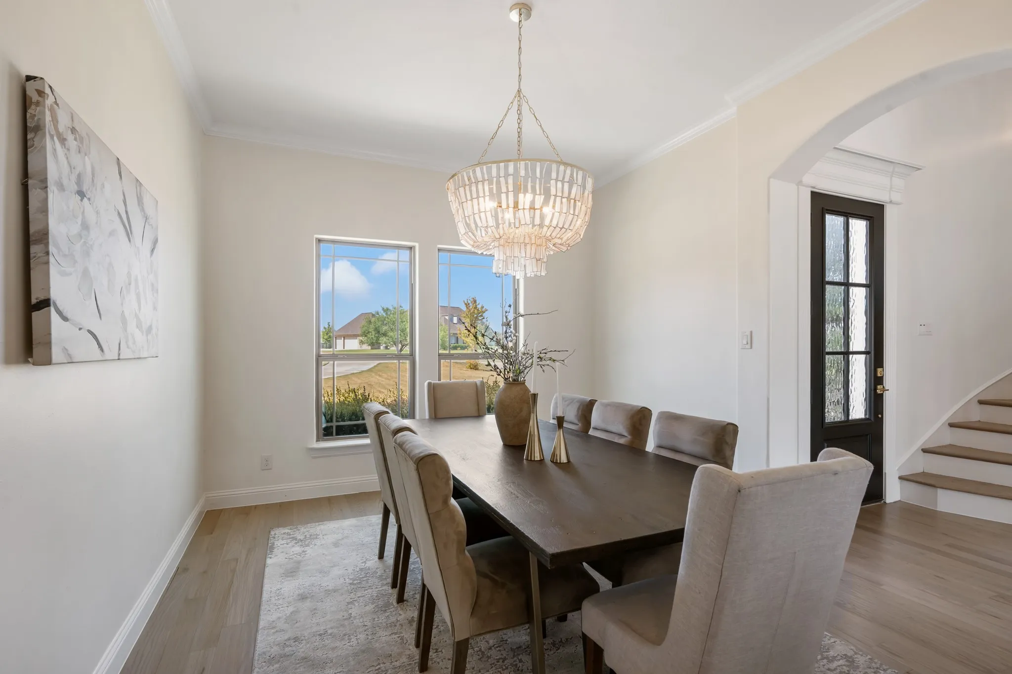 Crown molding throughout, wood-finish flooring, arched doorway, elegant chandelier, and a black-paneled door with frosted glass