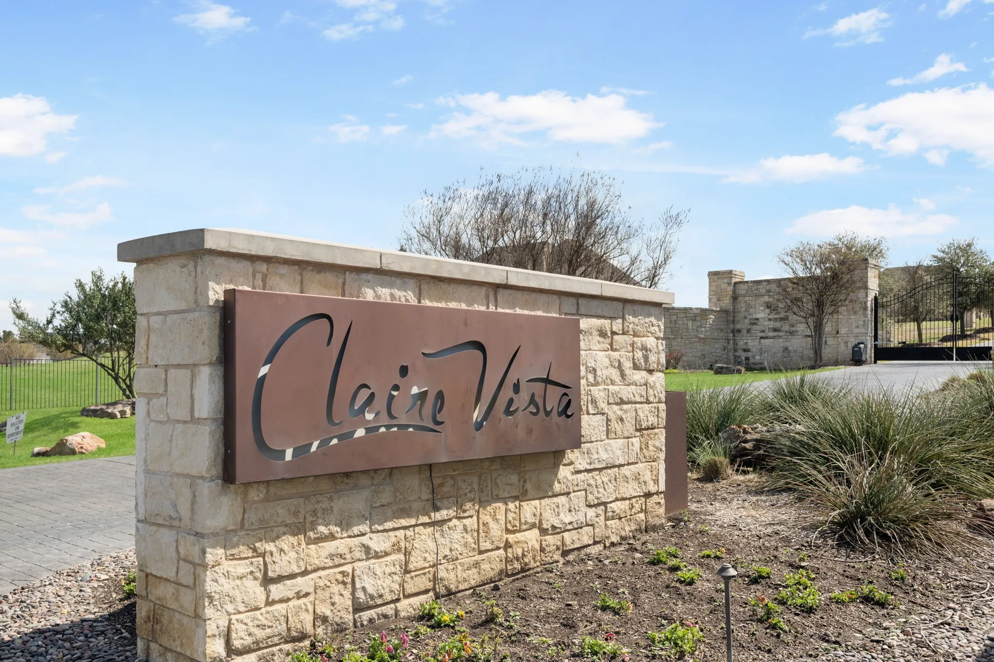 Stone entry monument with a decorative metal sign and integrated landscaping